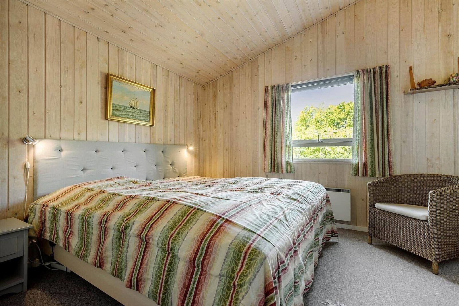 Schlafzimmer mit Holzwand, Bett, Fenster und Stuhl.