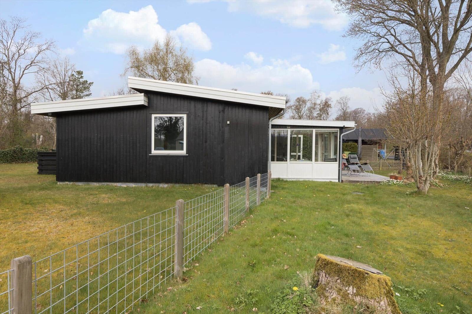 Black wooden house with white windows and terrace in the garden.