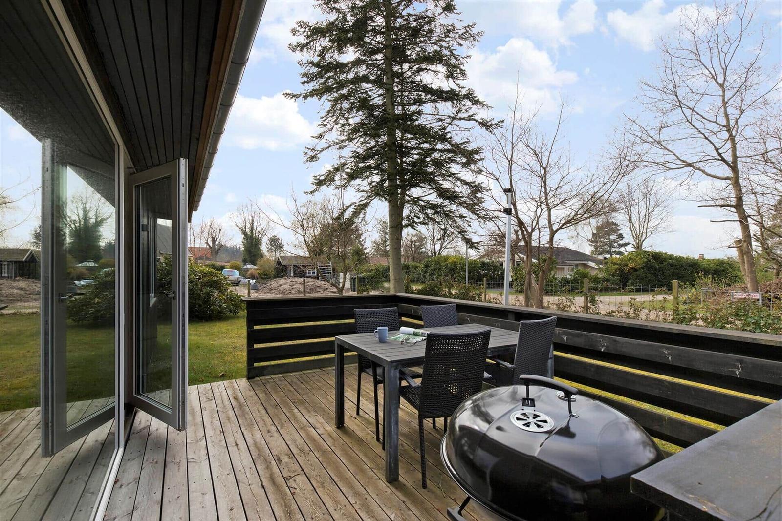 Deck with table, chairs, and grill. View of lawn and trees.