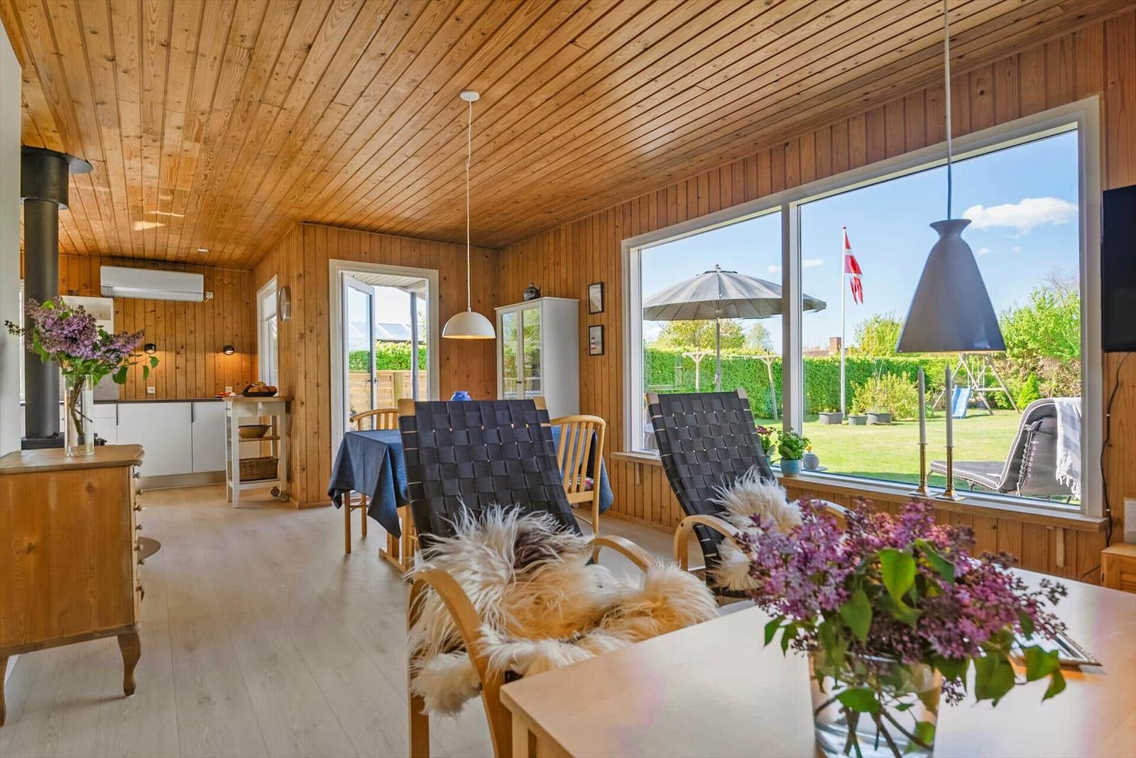 Wohnraum mit Holzwand, Sitzgelegenheiten und Blick auf Garten.