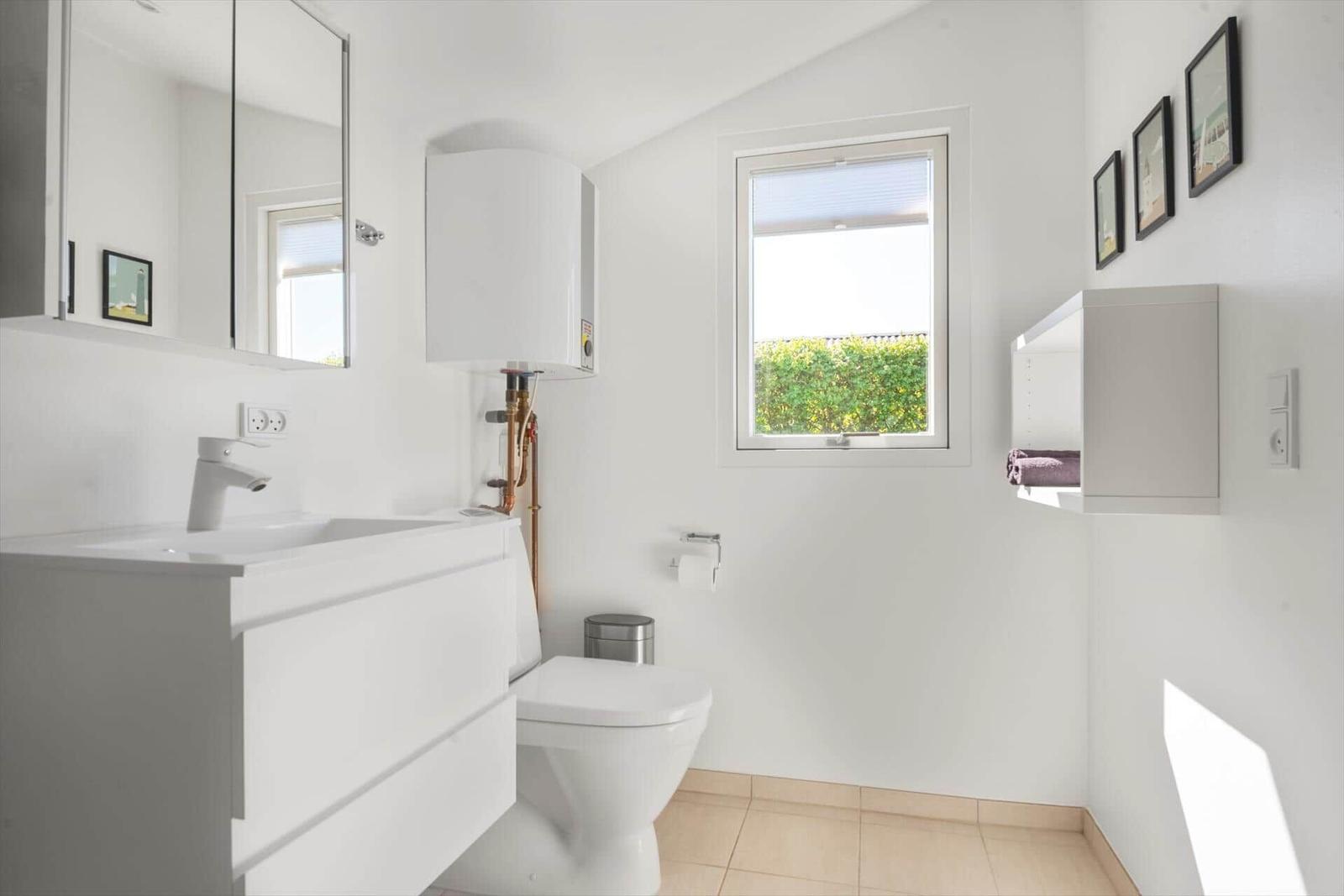 Badezimmer mit Waschbecken, Toilette und Fenster zur grünen Außenseite.