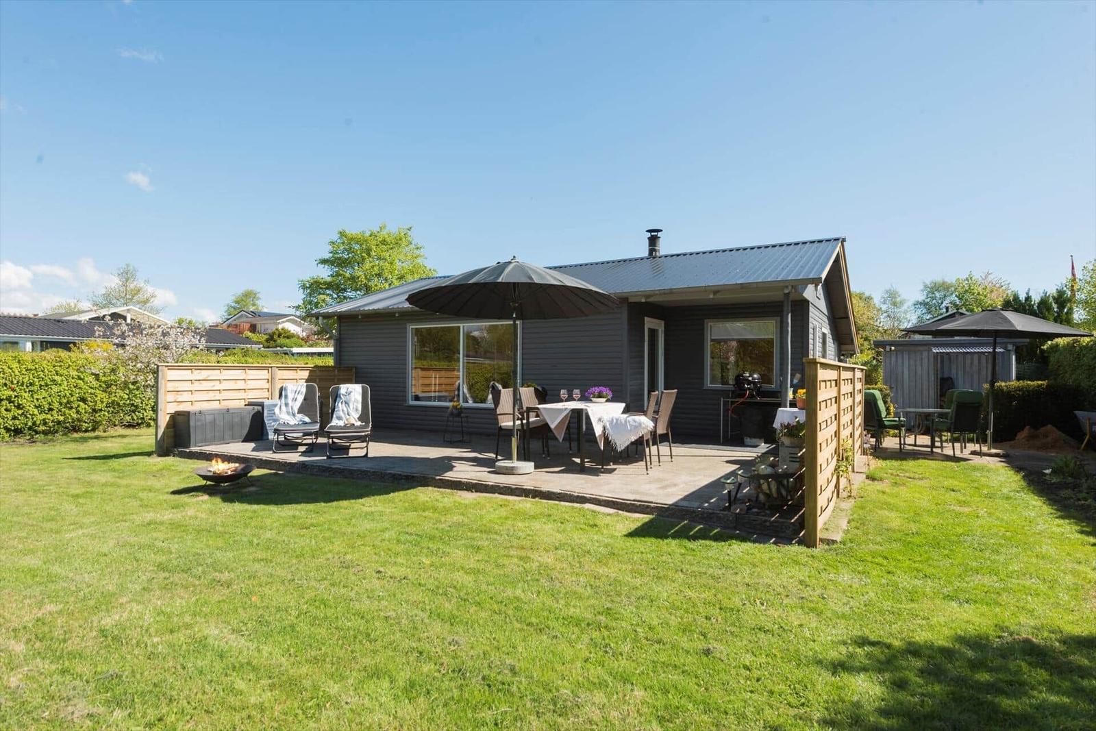 Haus mit Terrasse, Garten und Sitzgelegenheiten unter Sonnenschirm.