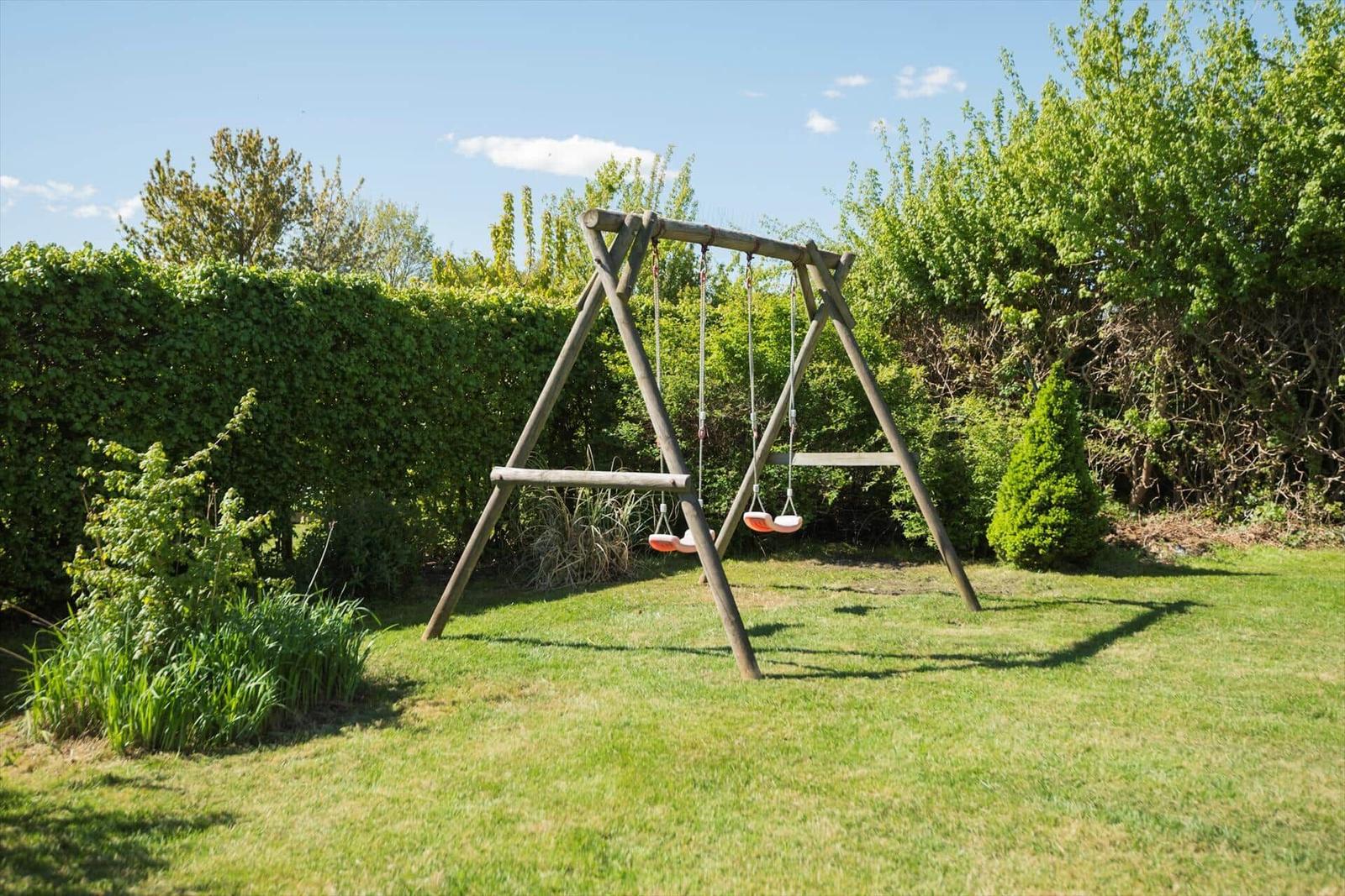 Holzschaukel mit zwei Sitzplätzen im grünen Garten.