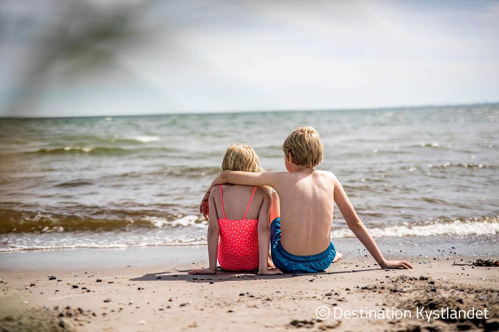 Zwei Kinder sitzen am Strand und schauen aufs Meer.