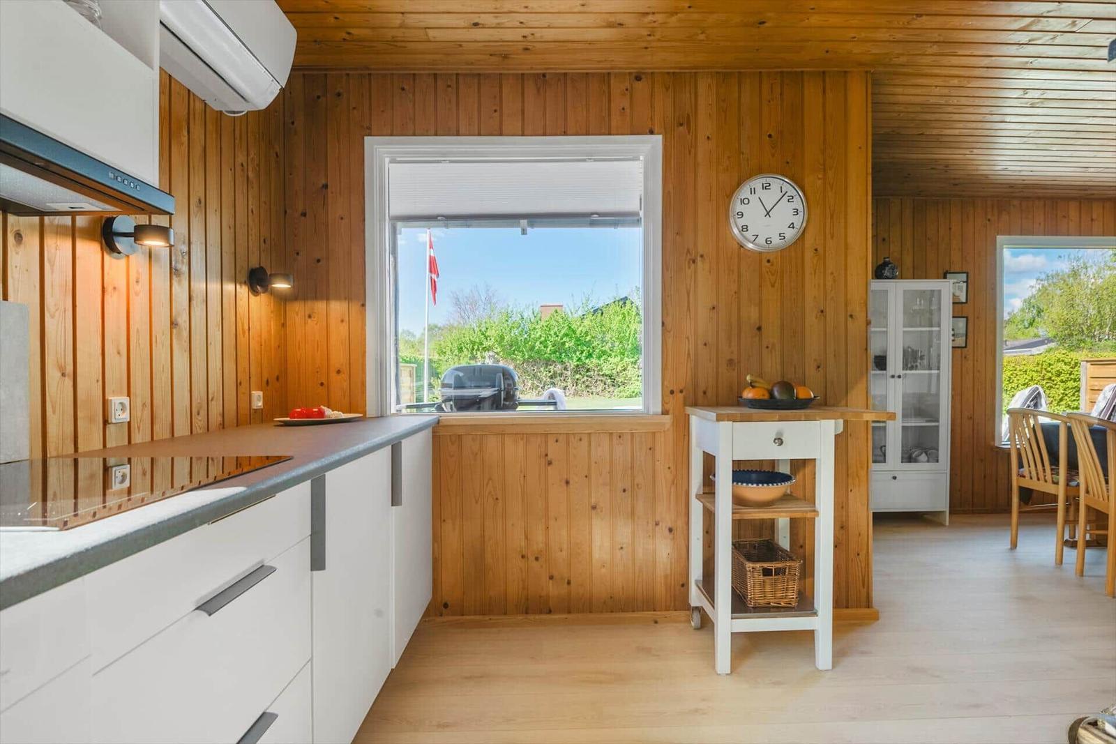 Küche mit Holzwand und Blick auf Garten. Weiße Schränke und Kücheninsel.