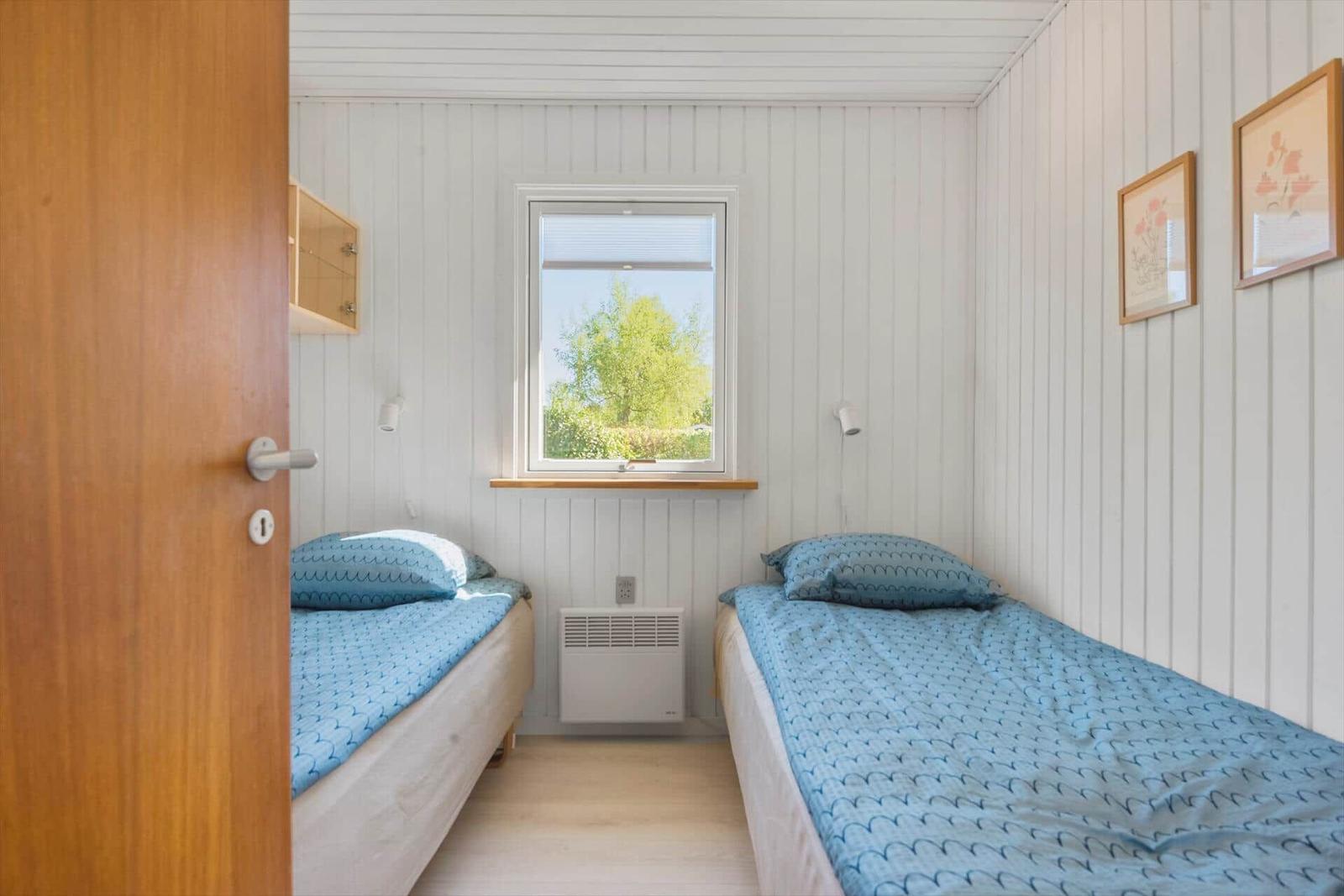 Zwei Einzelbetten mit blauen Bettwäschen, Fenster mit Blick auf Bäume, weiße Wandverkleidung.