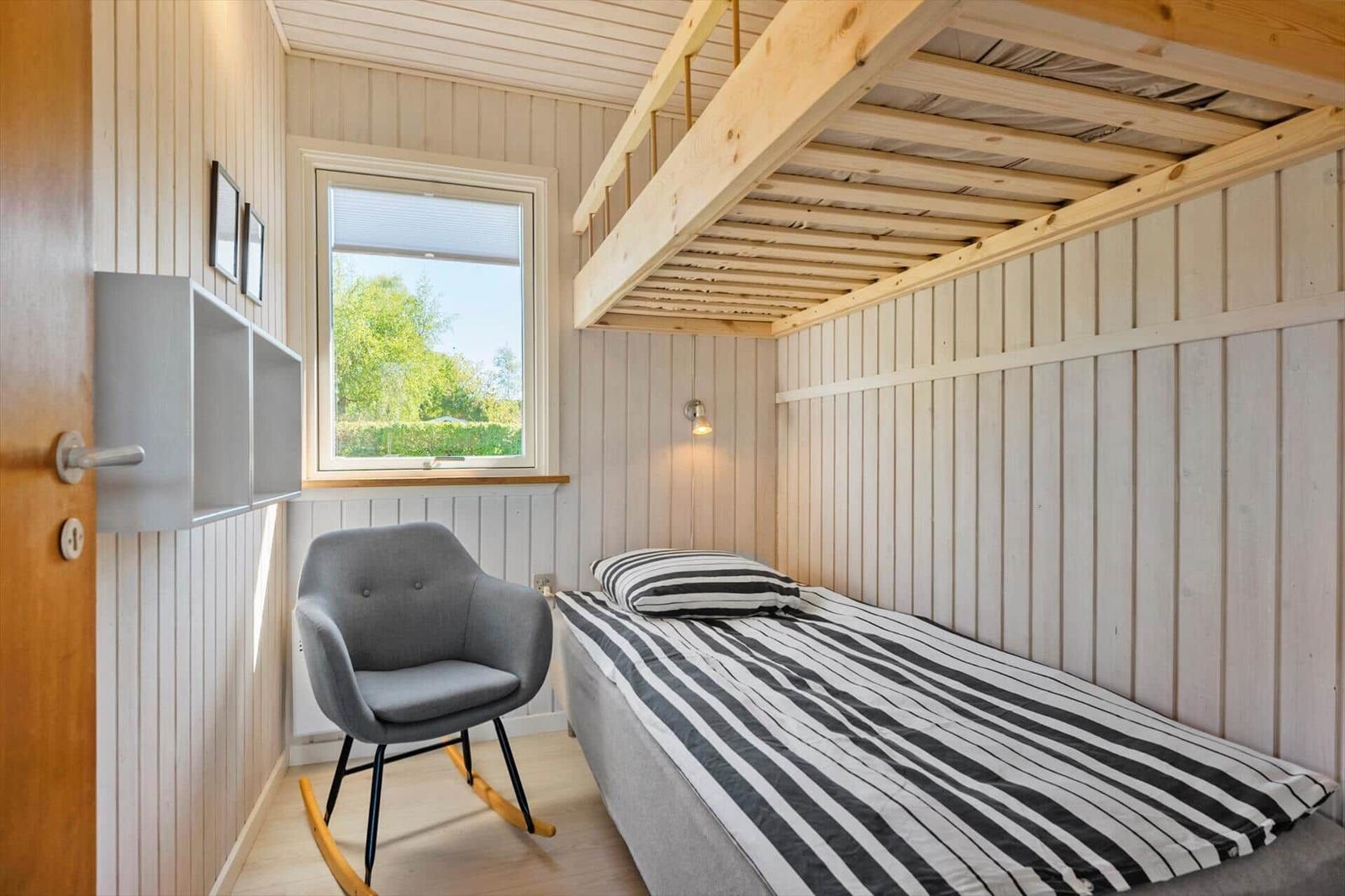 Ein Schlafzimmer mit Bett, Stuhl und Fenster. Holzdecke und Wandverkleidung.