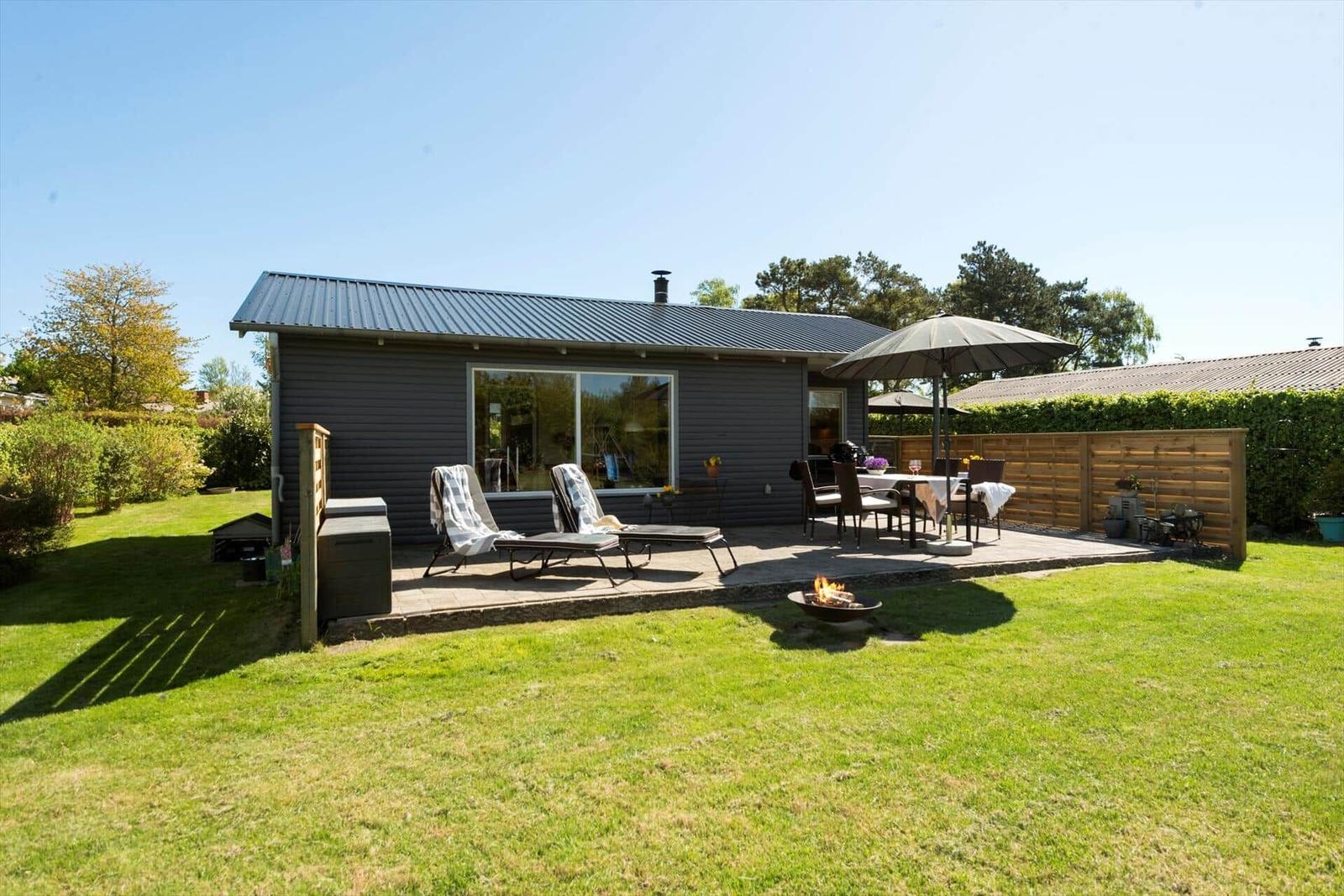 Haus mit Terrasse, Liegestühlen, Tisch und Grillplatz im Garten.