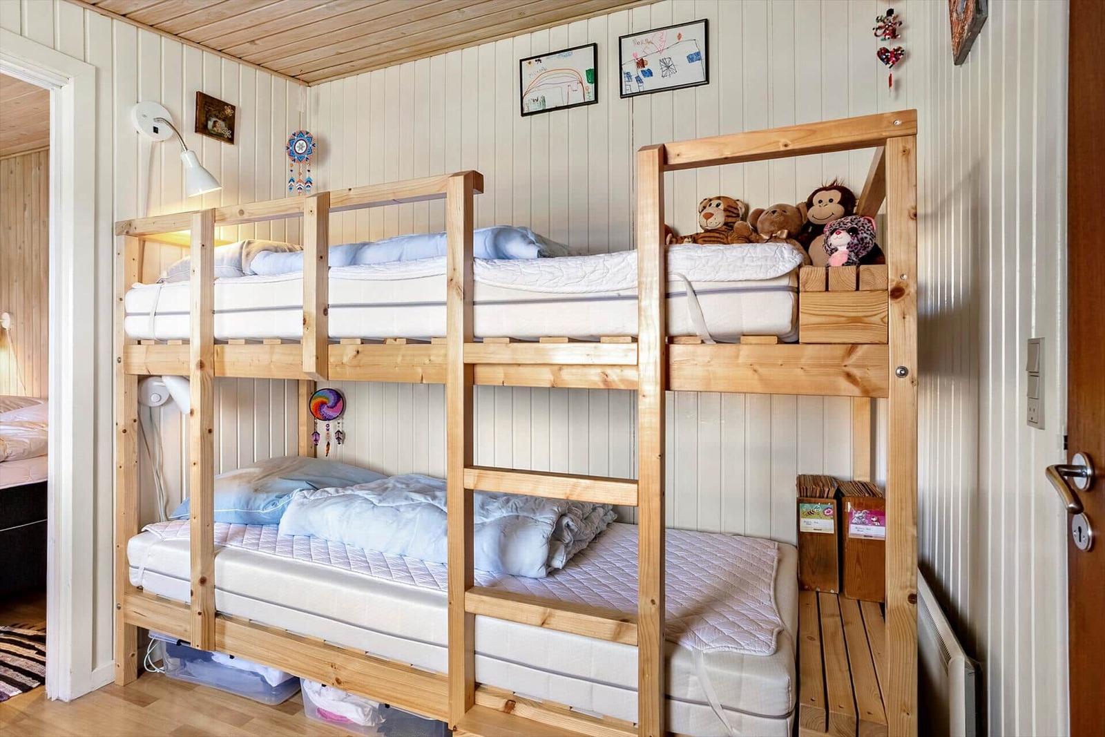 Zwei hölzerne Etagenbetten mit Matratzen und Kissen. An der Wand hängen Bilder und Dekorationen.