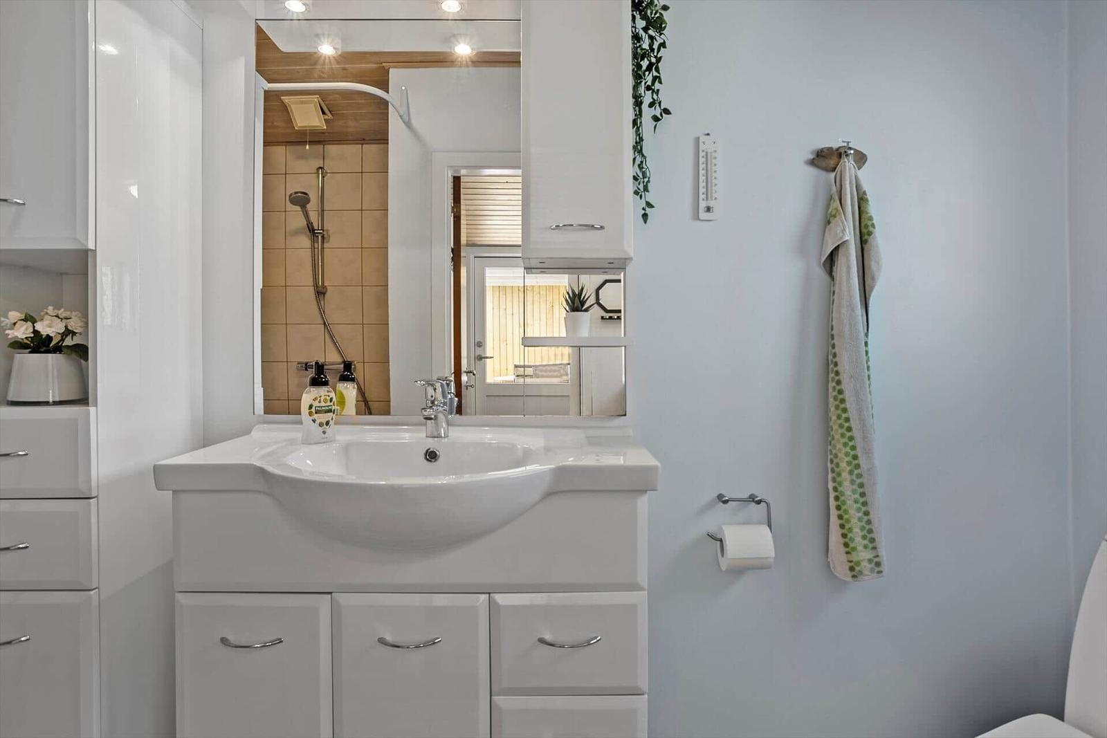 Badezimmer mit Waschbecken, Spiegel und Dusche. Handtuch und Toilettenpapier vorhanden.