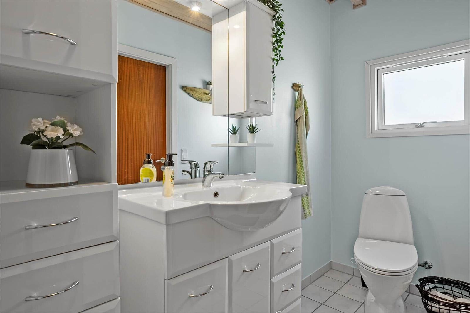 Badezimmer mit Waschbecken, Spiegel, Toilette und Fenster.