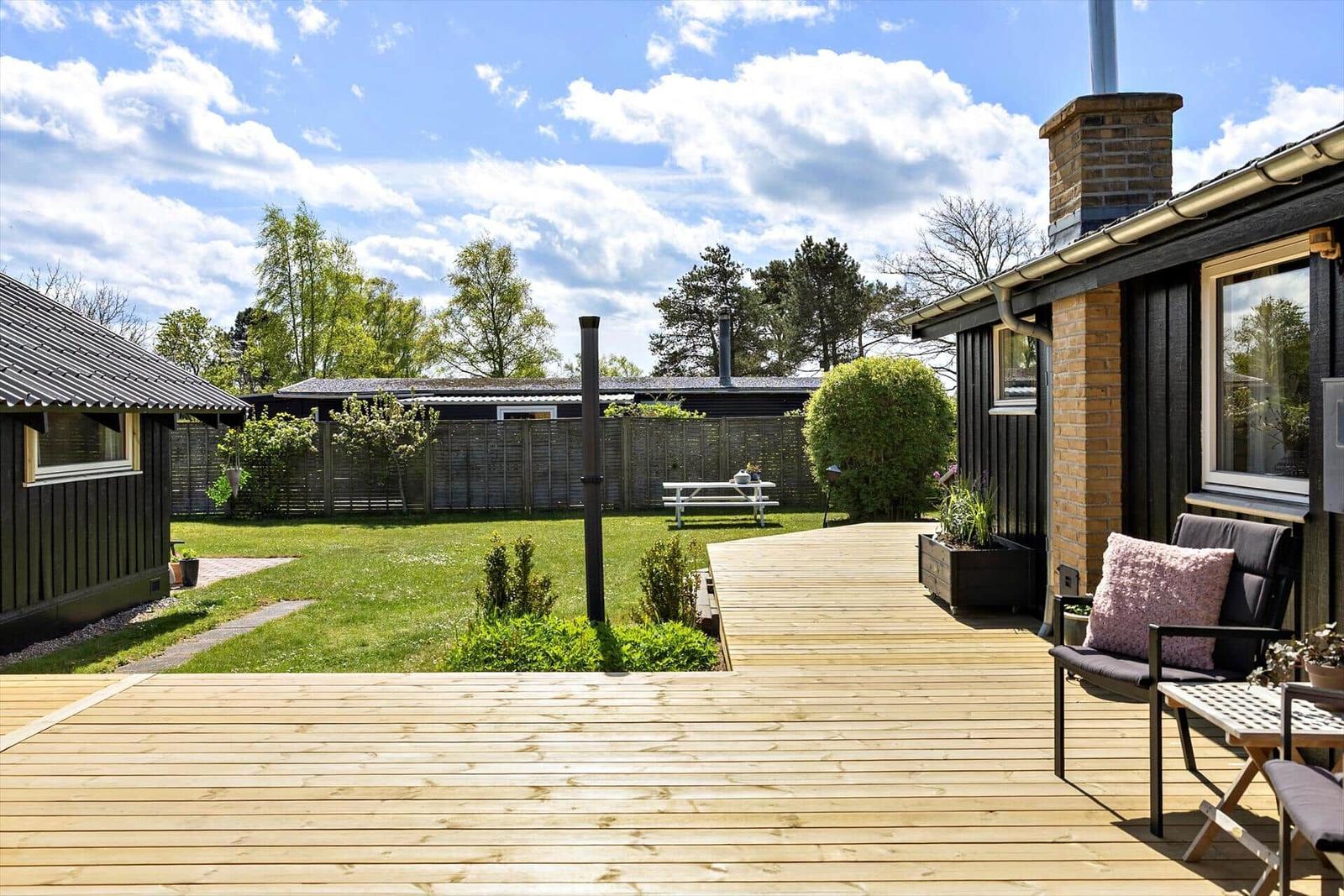 Holzterrasse mit Sitzgelegenheit, Garten und Blick auf Wald.