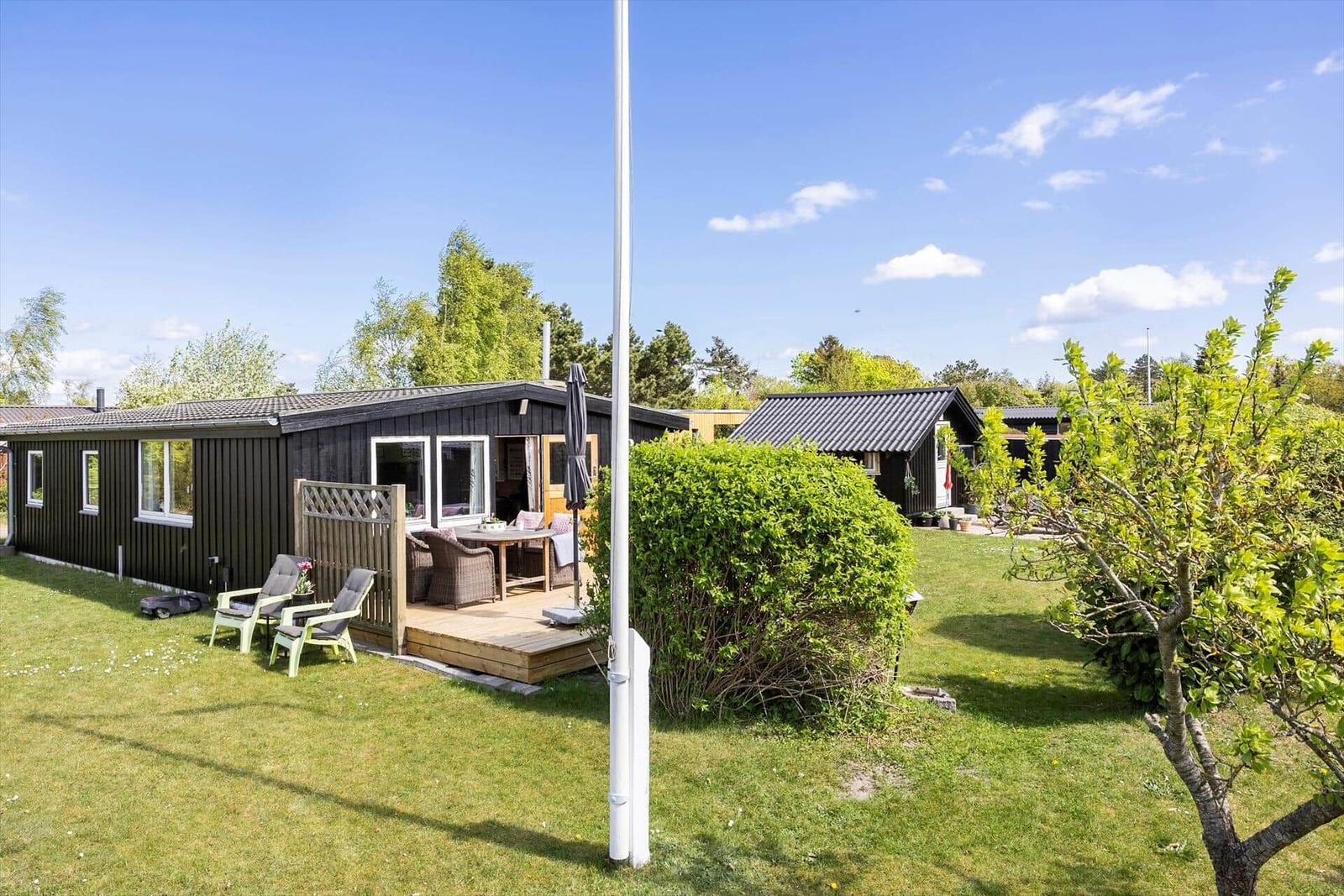 Ein Haus mit Terrasse, Garten und Bäumen unter blauem Himmel.