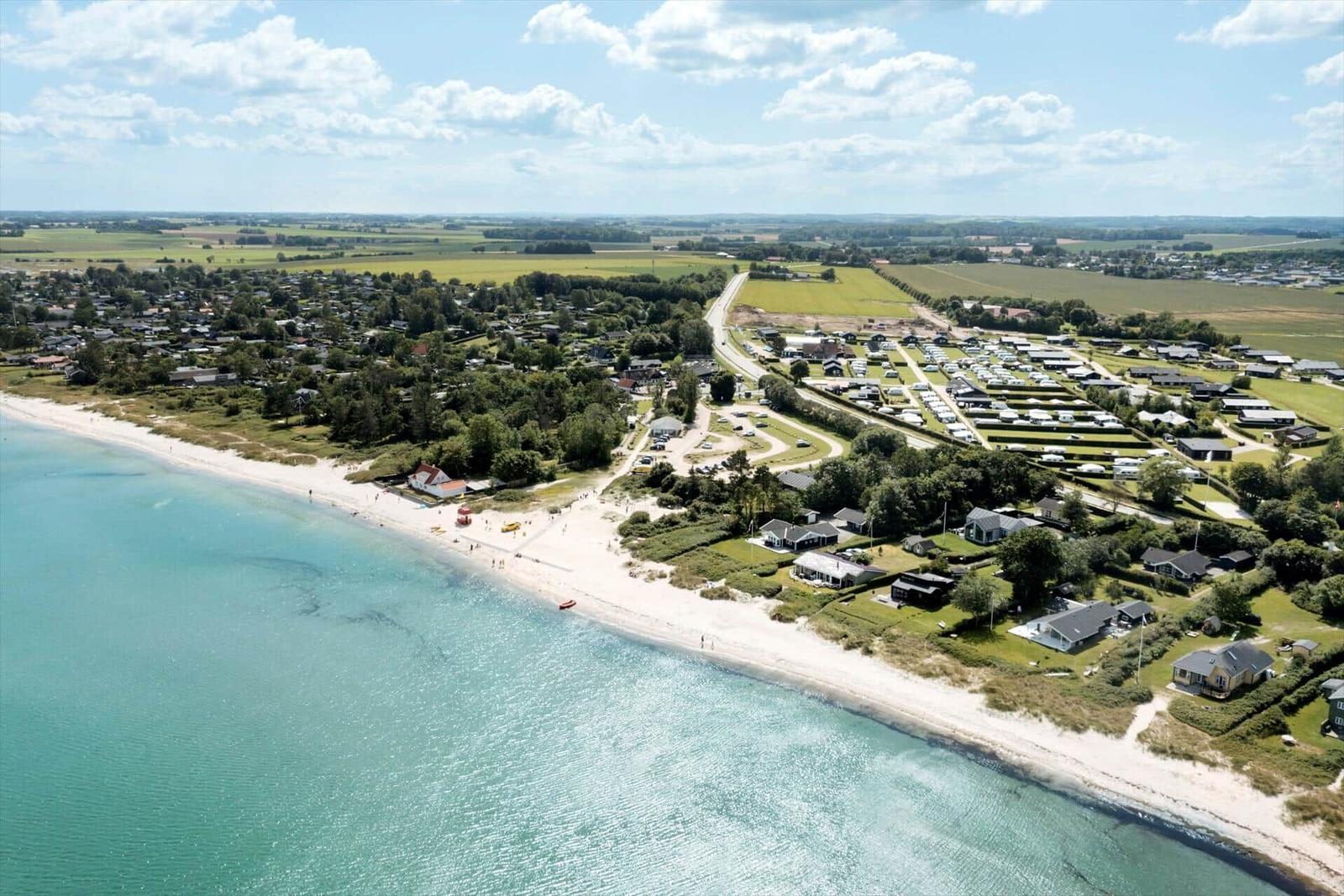 Strand mit Ferienhäusern und Campingplatz in ländlicher Umgebung.