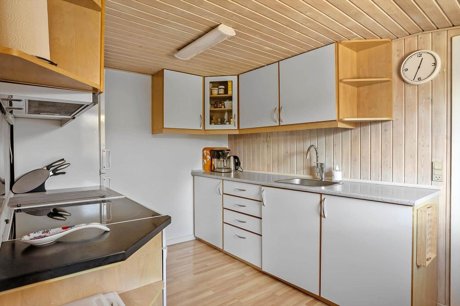Küche mit Holzdecke, weißen Schränken und Edelstahlspüle.