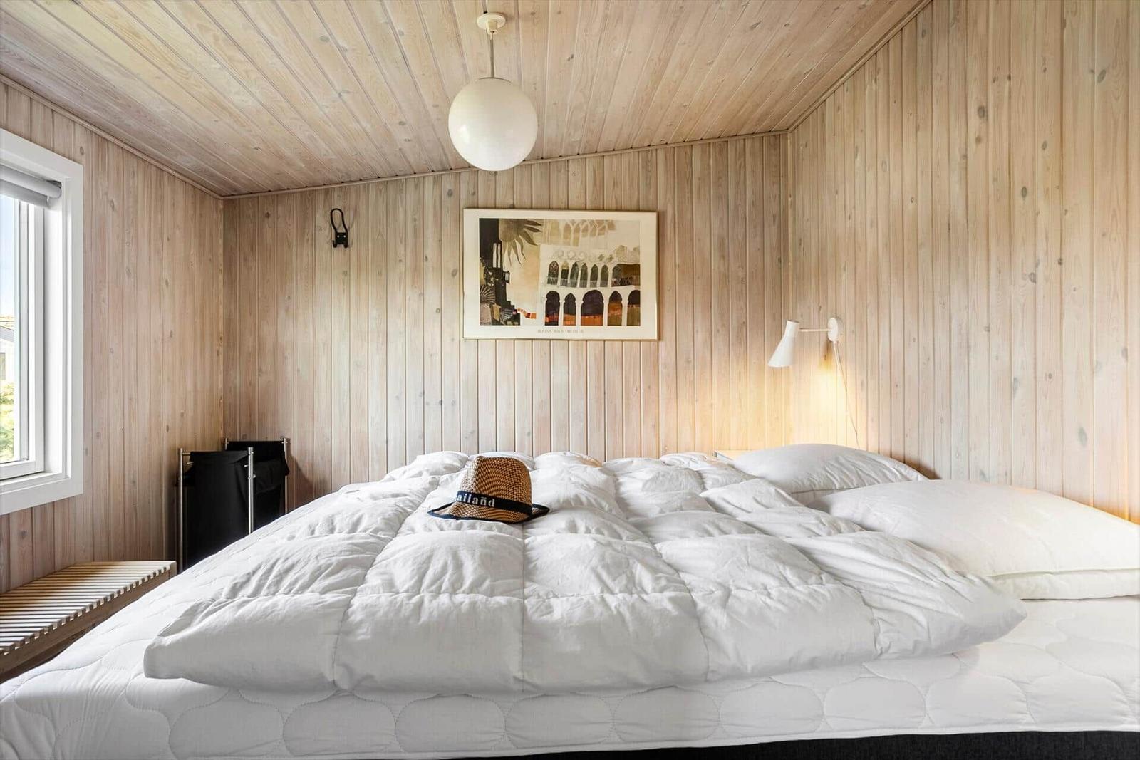 Schlafzimmer mit Holzwand, Bett und Fenster.