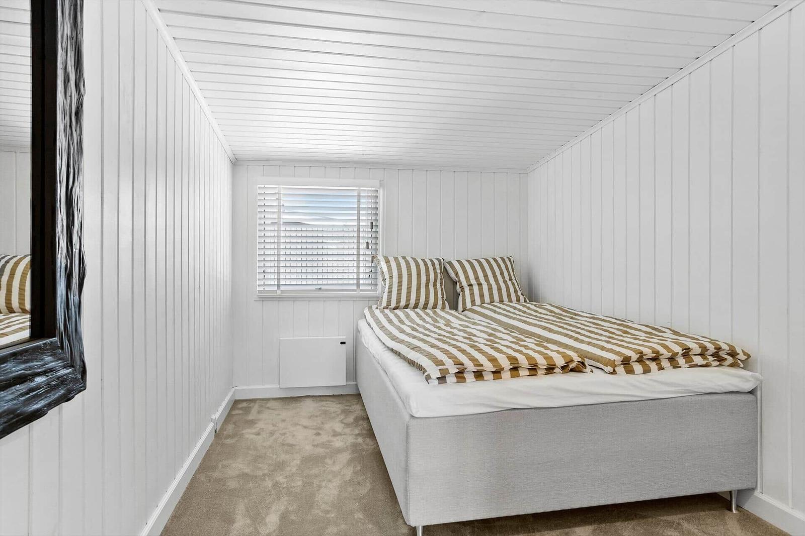 Schlafzimmer mit Bett, Fenster und Wandverkleidung.