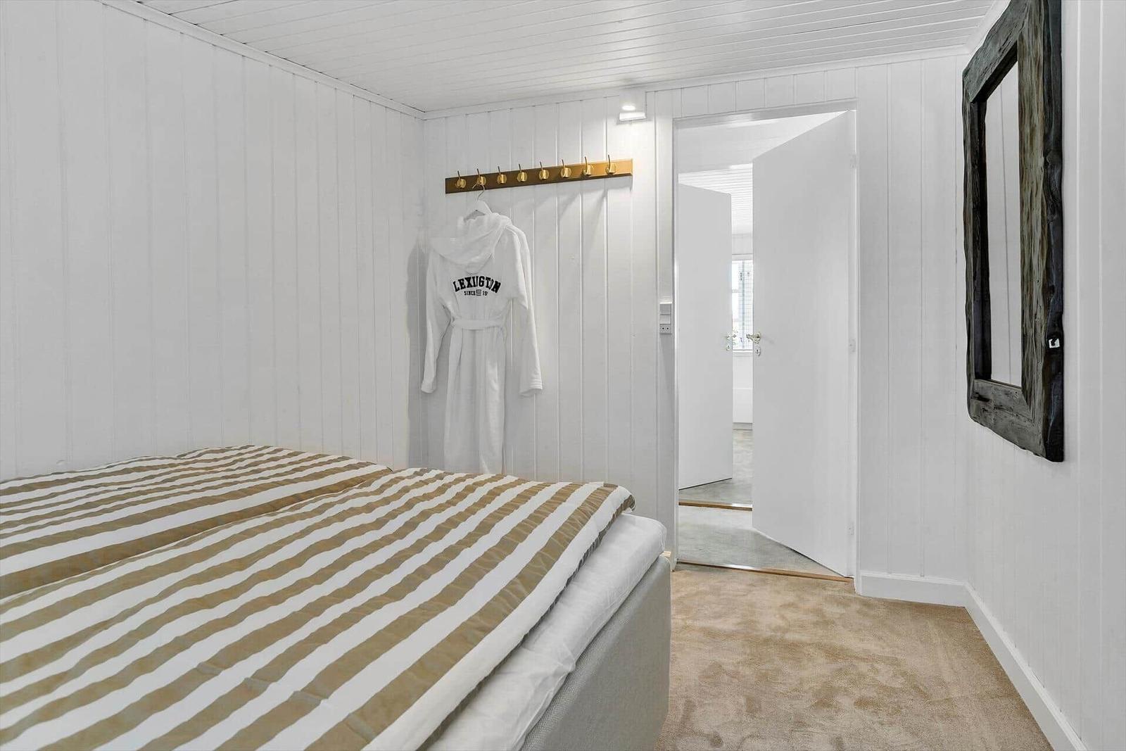 Schlafzimmer mit Bett, Bademantel an Haken und Spiegel an der Wand.