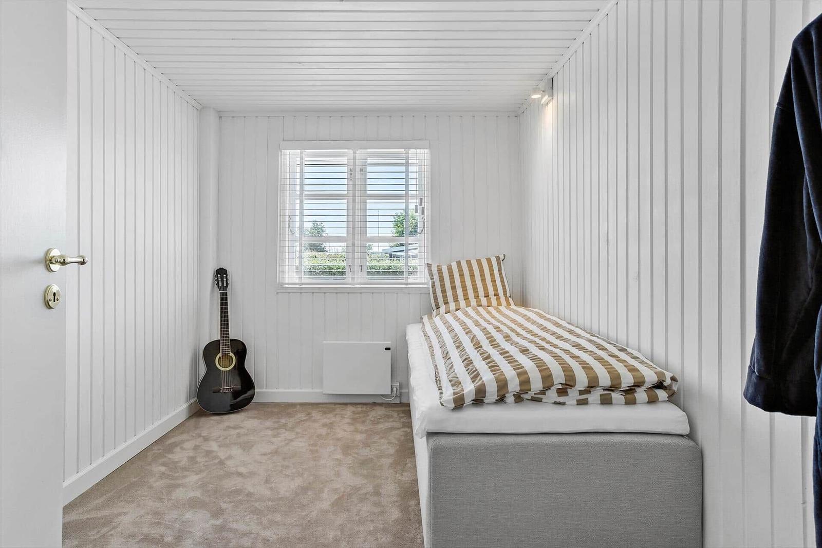 Schlafzimmer mit Bett, Fenster und Akustikgitarre.