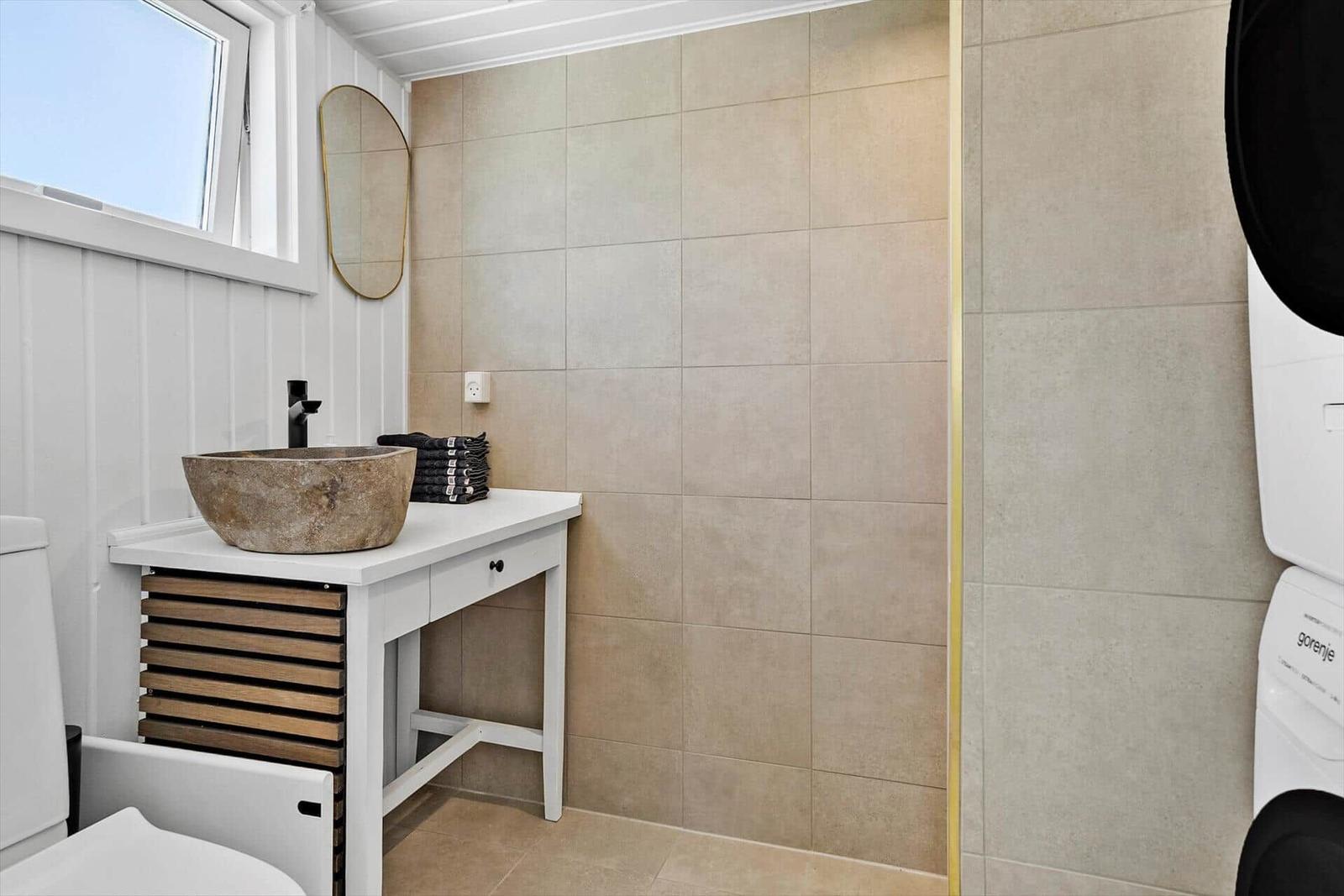 Badezimmer mit Waschtisch, Spiegel und Toilette. Wandfliesen und Holzelemente.