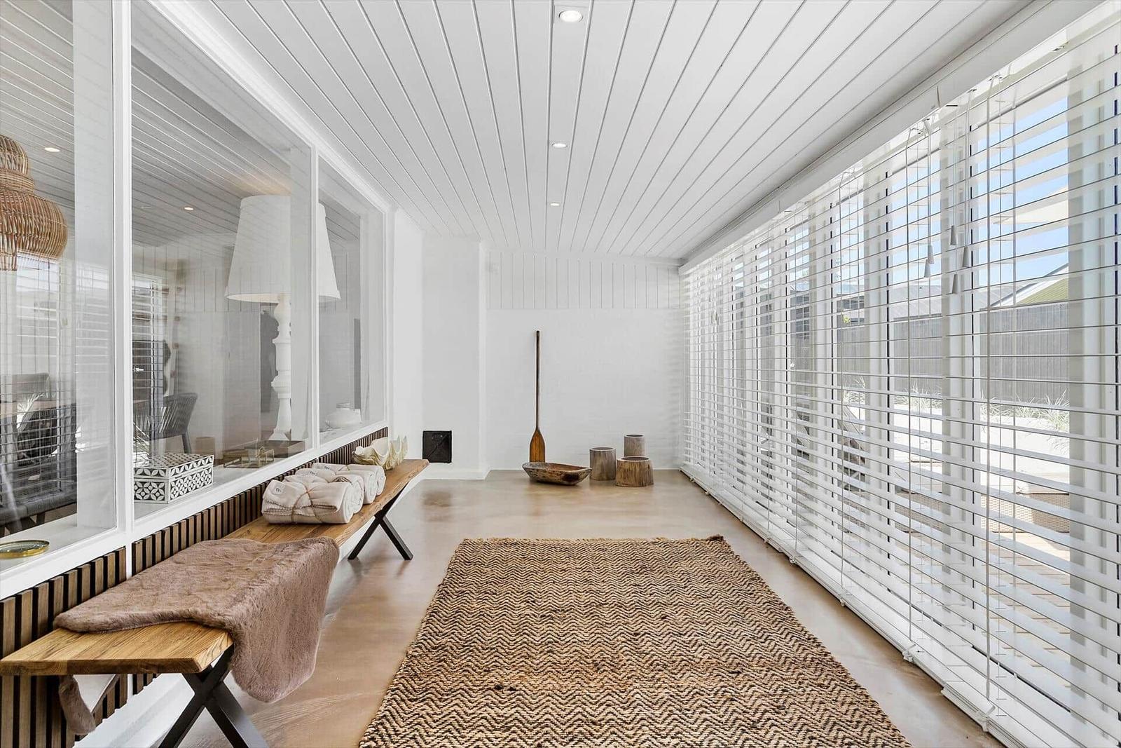 Lange Halle mit weißen Wänden, Holzboden und großen Fenstern mit Jalousien.