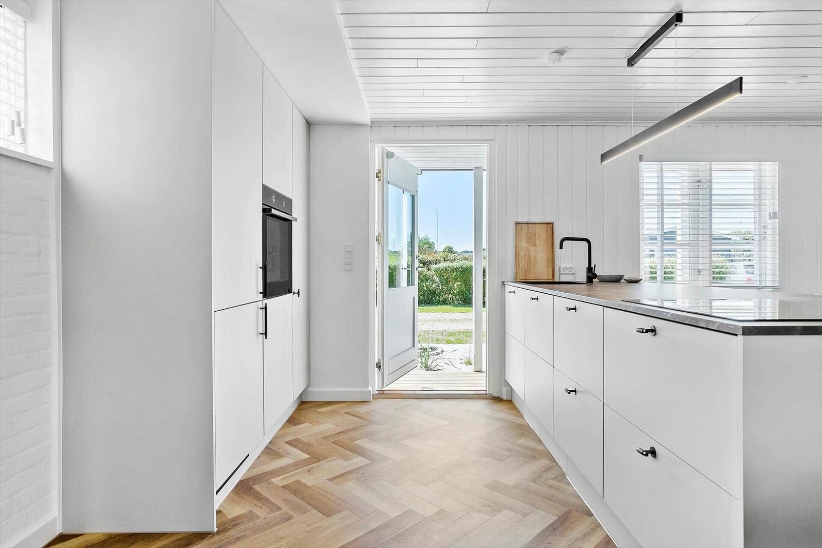 Moderne Küche mit weißer Einbauküche, Holzboden und Blick auf den Garten.