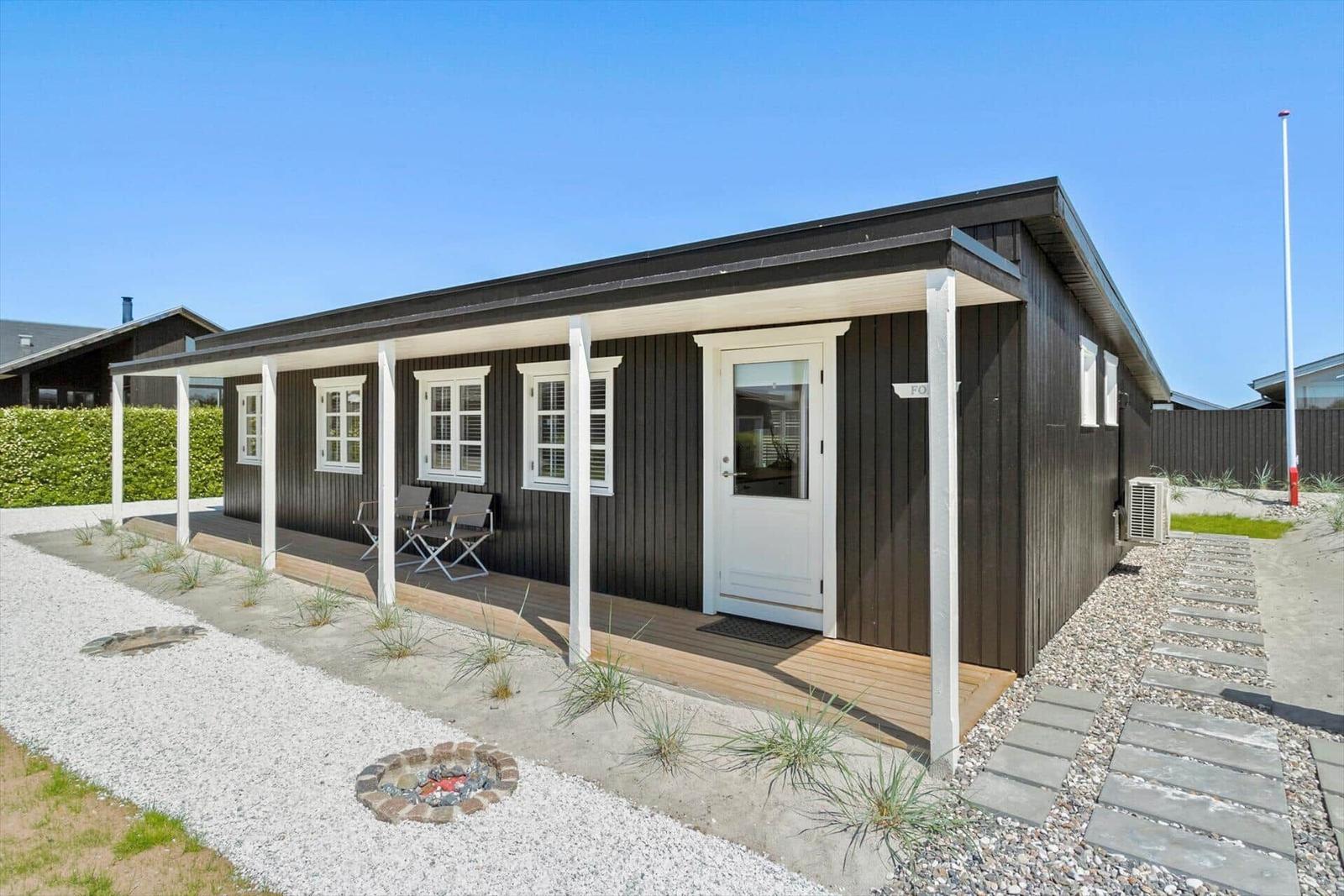 Moderne Holzhütte mit Veranda, Garten und Feuerstelle.