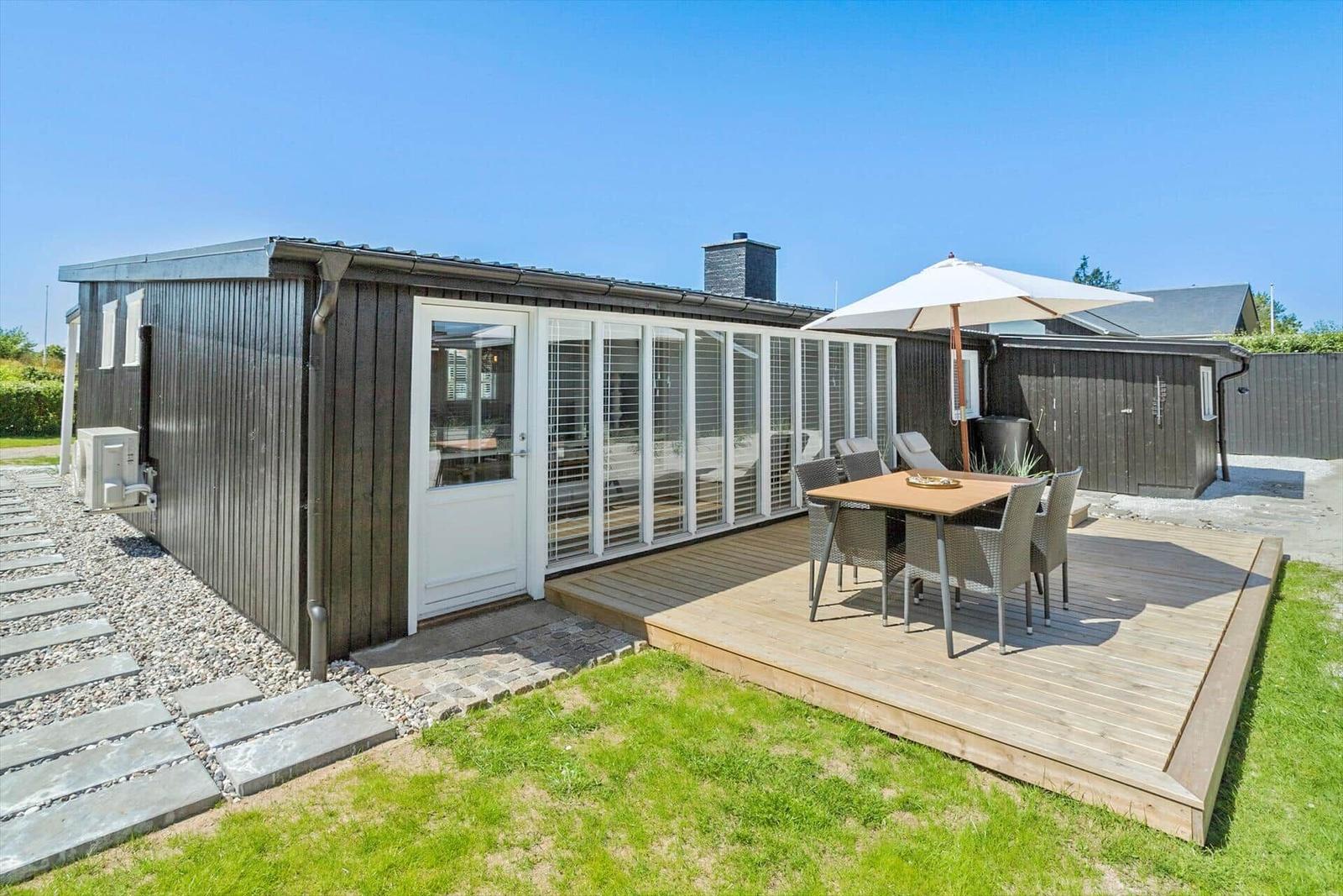 Moderne Villa mit Terrasse, Garten und Sitzgruppe unter Sonnenschutz.