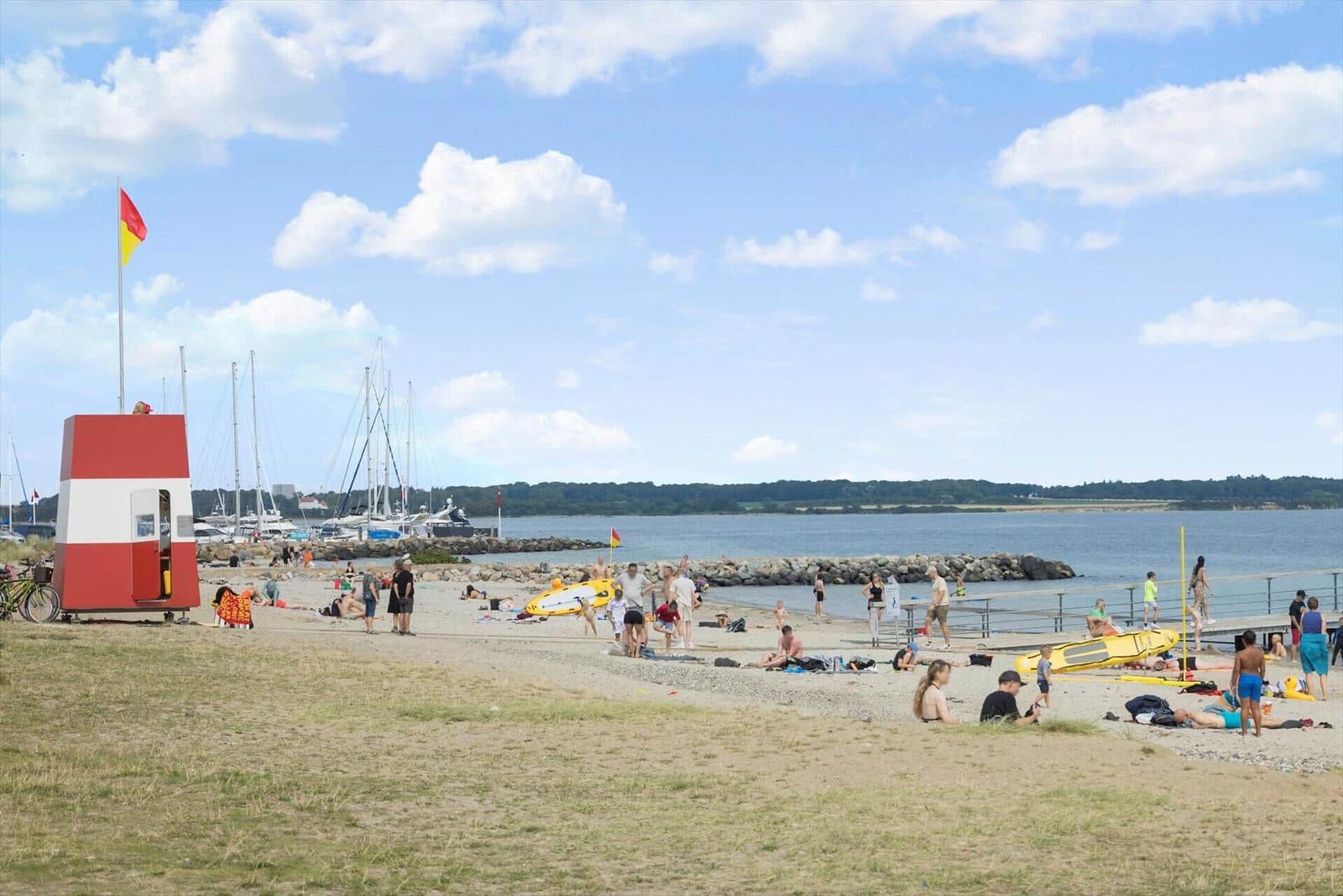 Strand mit Badegästen, Rettungswache und Booten im Hintergrund.