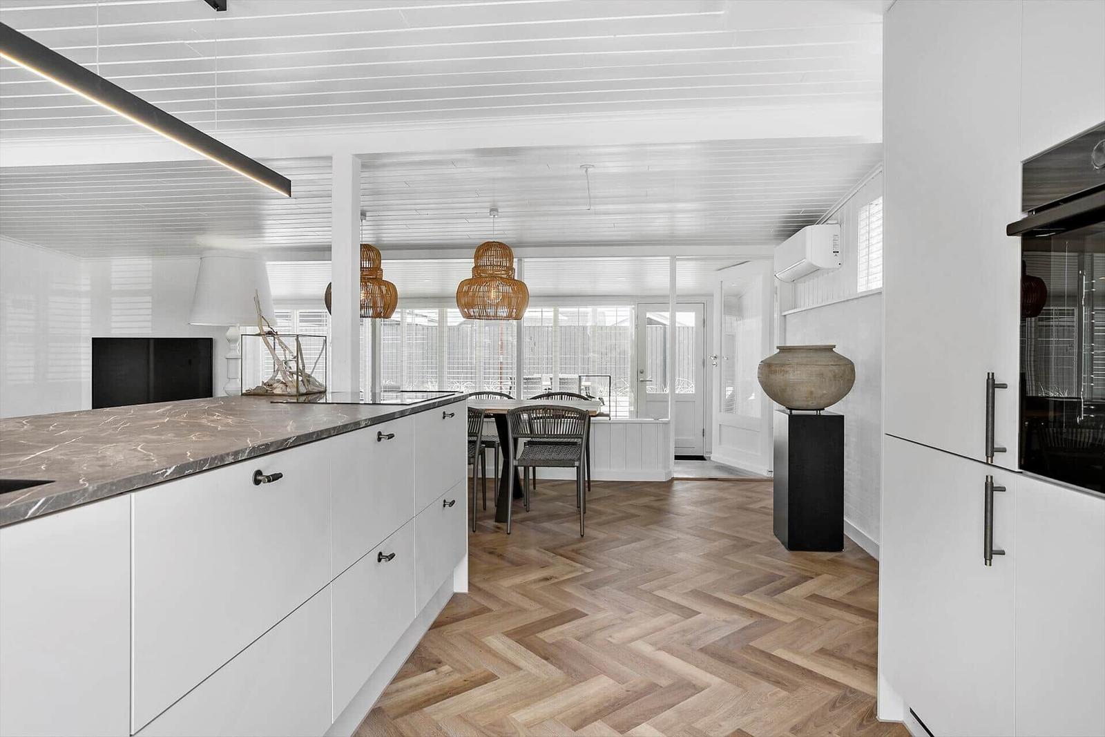 Moderne Küche mit weißem Schrank und Marmorarbeitsplatte. Holzfußboden und Essbereich im Hintergrund.