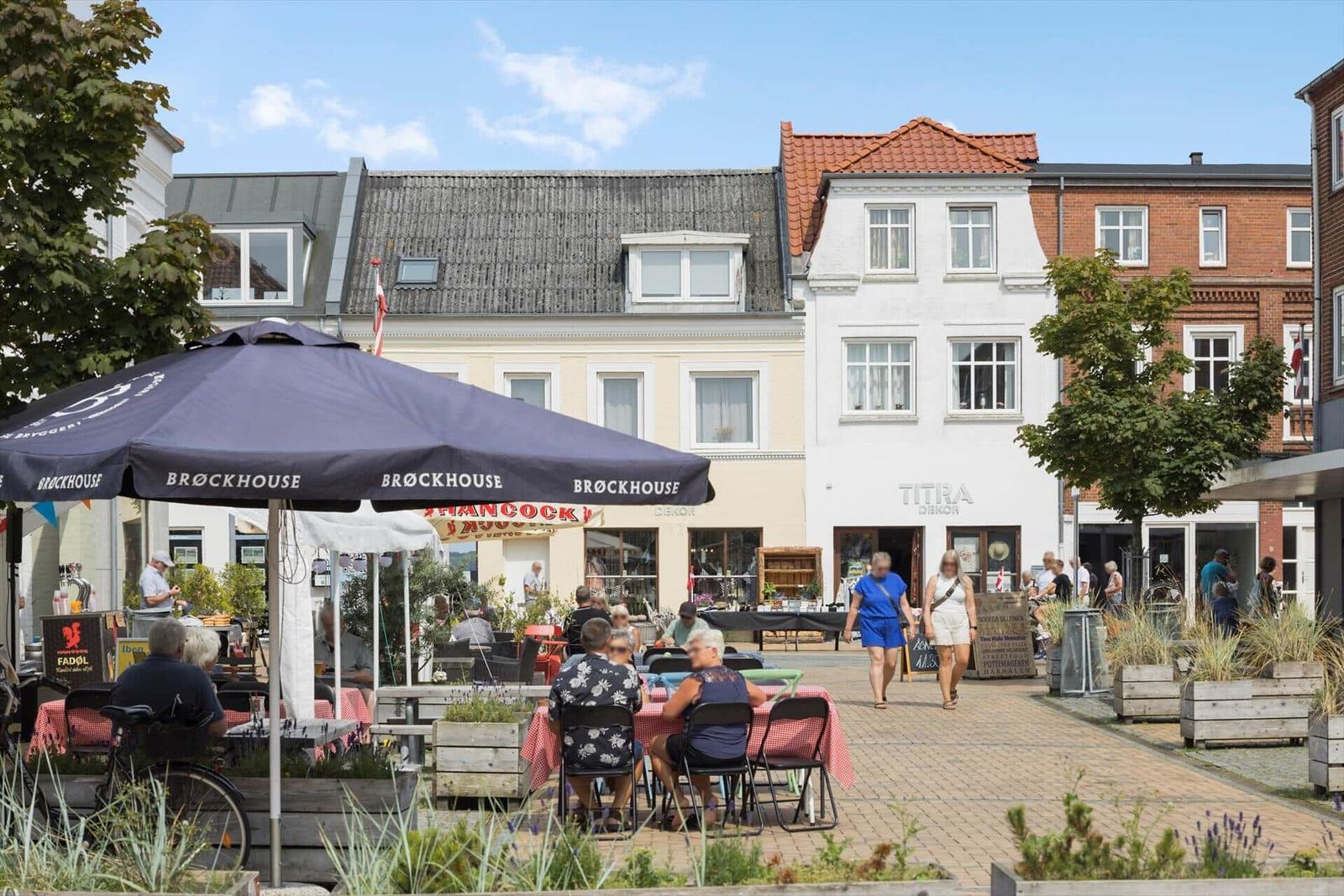 Außenbereich mit Tischen, Sonnenschirmen und Passanten vor historischen Gebäuden.