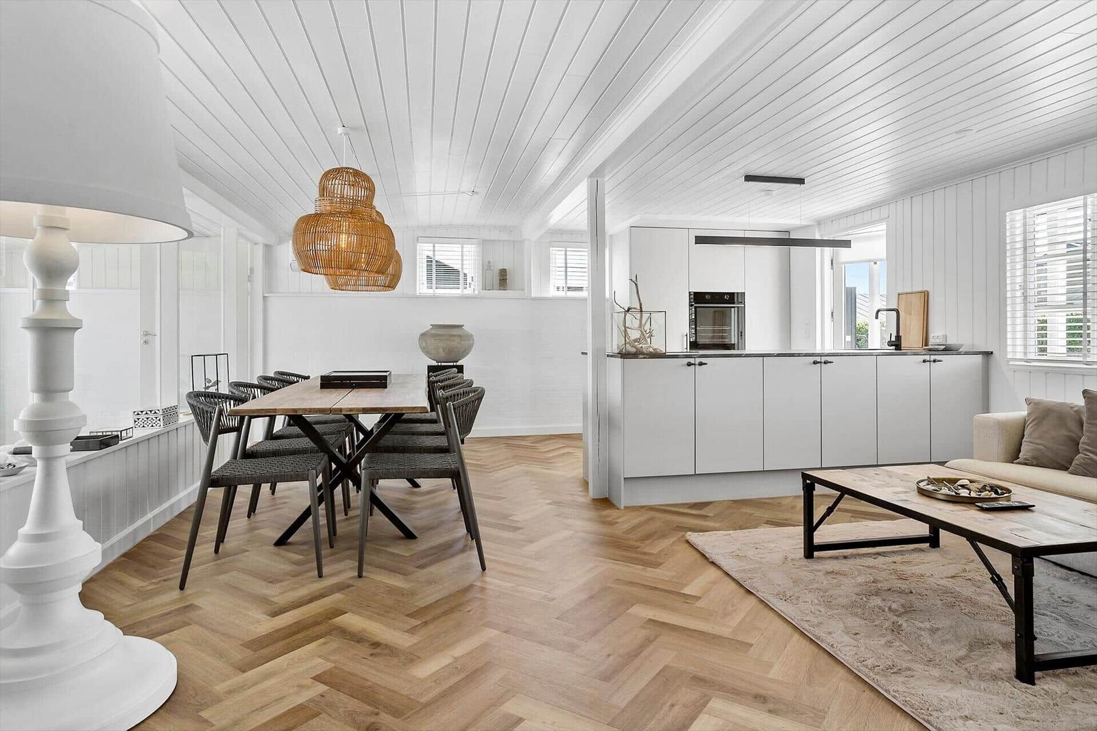 Wohn- und Essbereich mit Holzboden, weißer Küche und Esstisch mit Stühlen.