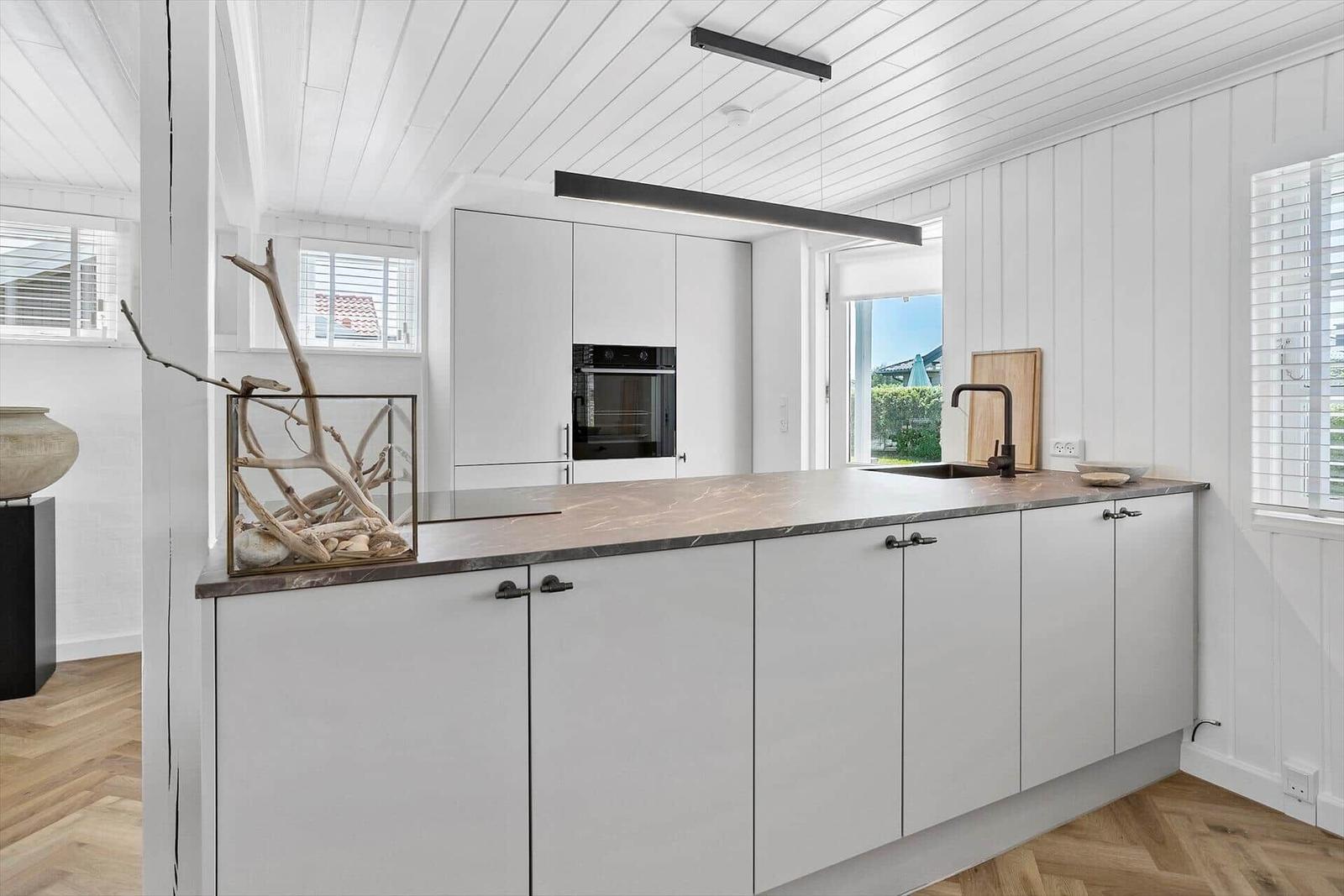 Moderne Küche mit weißen Schränken, Steinplatte und integriertem Ofen.