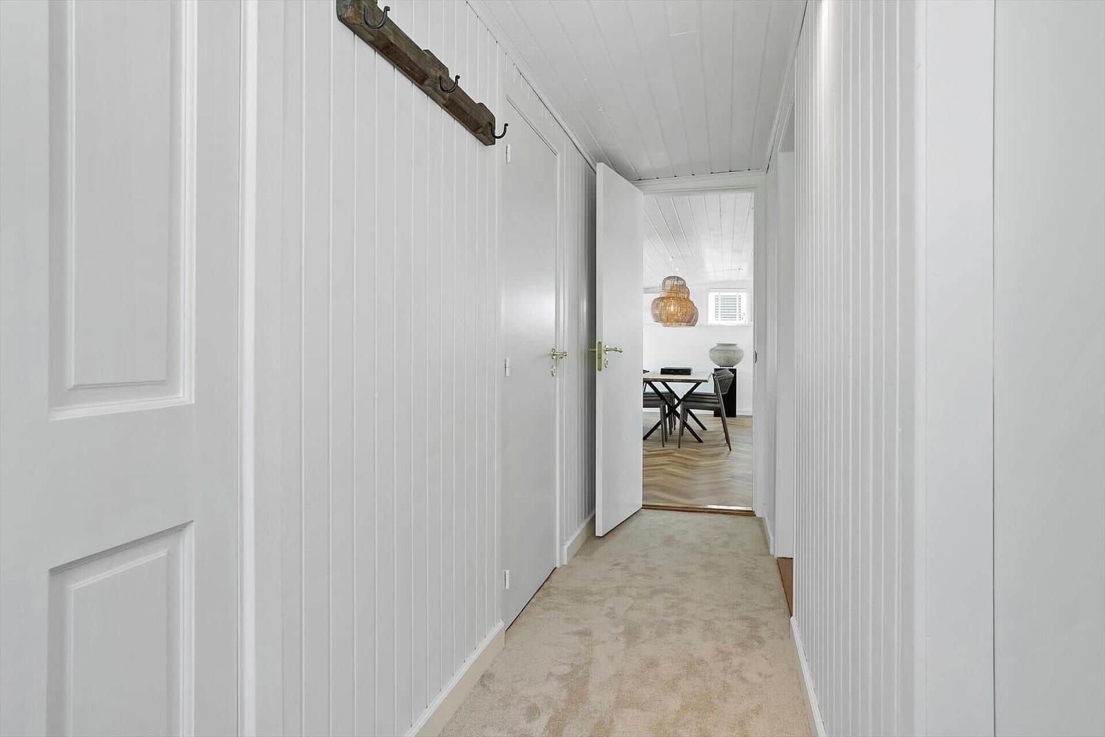 Flur mit weißen Wänden und Teppichboden. Durchgang zu Esszimmer mit Tisch und Lampe.