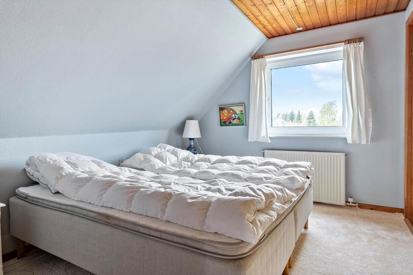 Schlafzimmer mit Dachschrägen, Fenster und Bett.