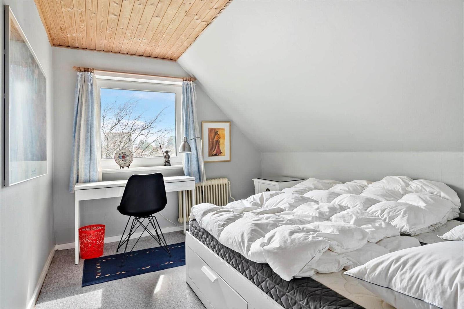 Schlafzimmer mit Dachschräge, Bett, Schreibtisch und Fenster.