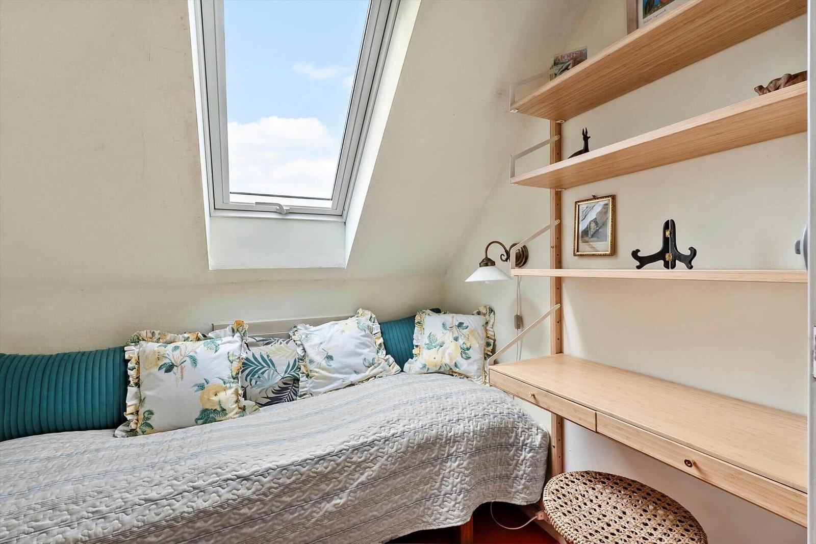 Dachgeschosszimmer mit Dachfenster, Bett und Schreibtisch.