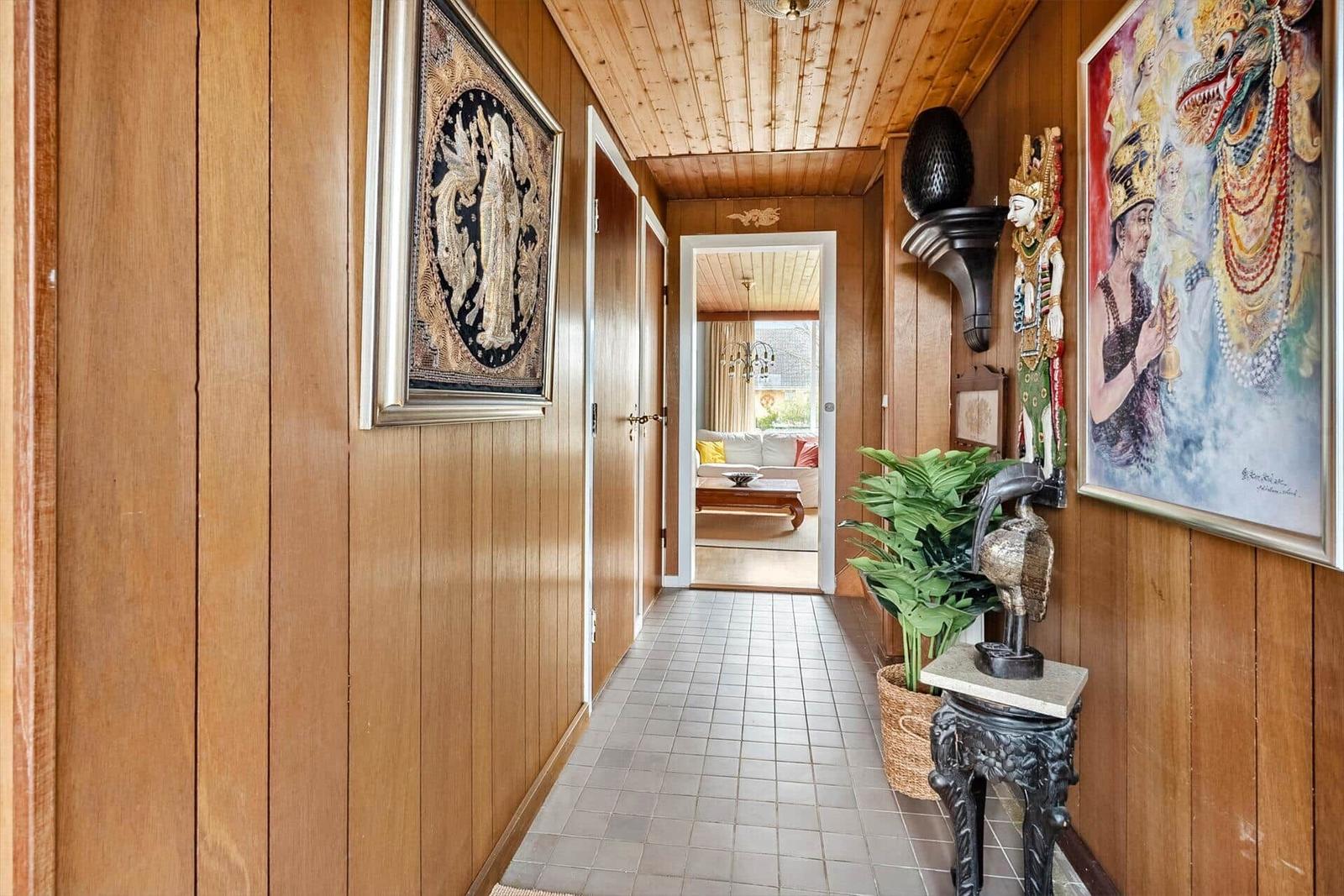Flur mit Holzwand, Kunstwerken und Pflanze. Durchgang in Wohnzimmer mit Sofa.