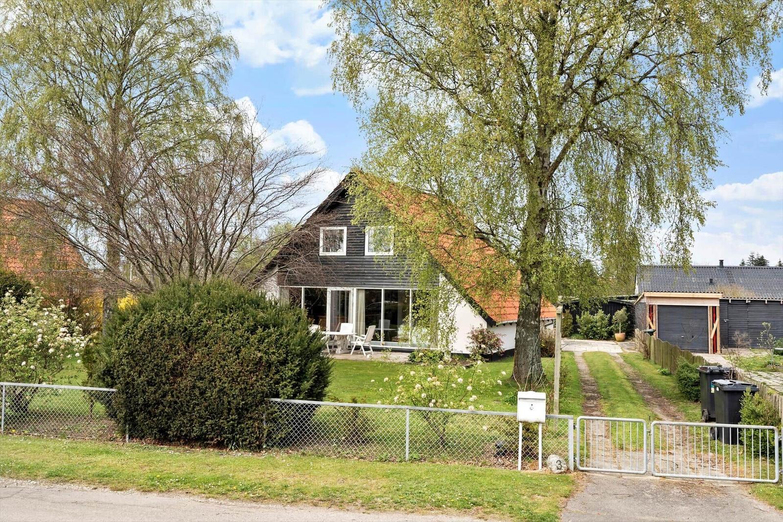 Haus mit Garten, Terrasse und Bäumen unter blauem Himmel.