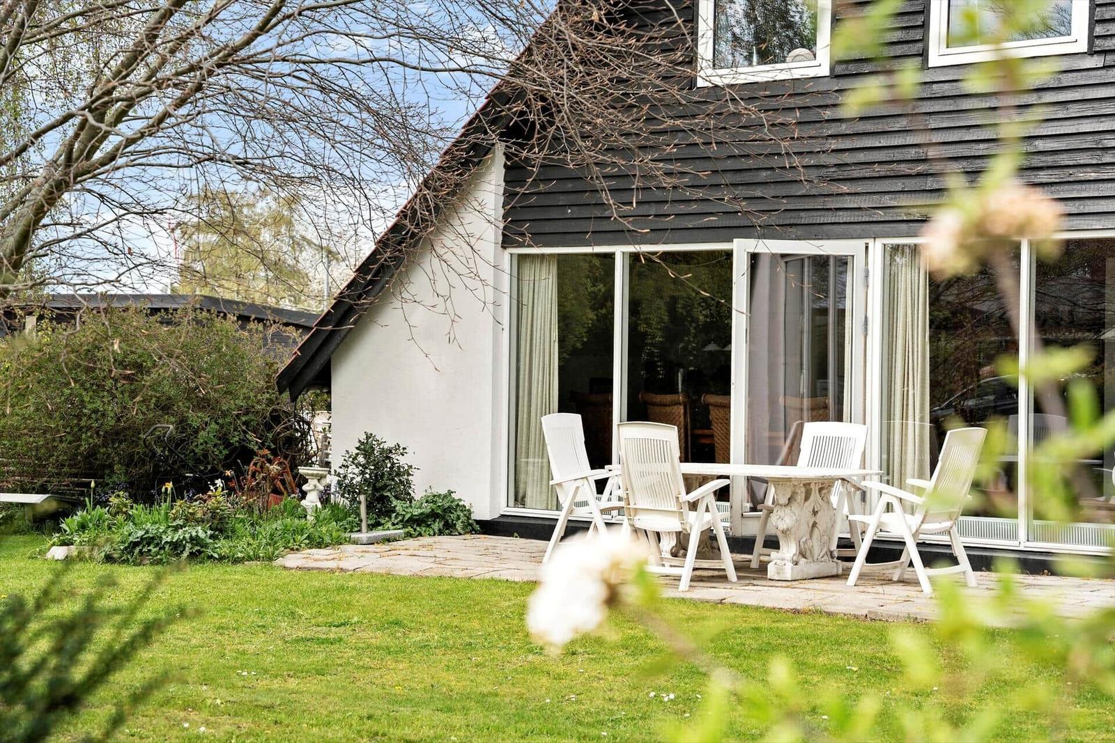 Haus mit Garten, Terrasse und weißem Tisch mit Stühlen.
