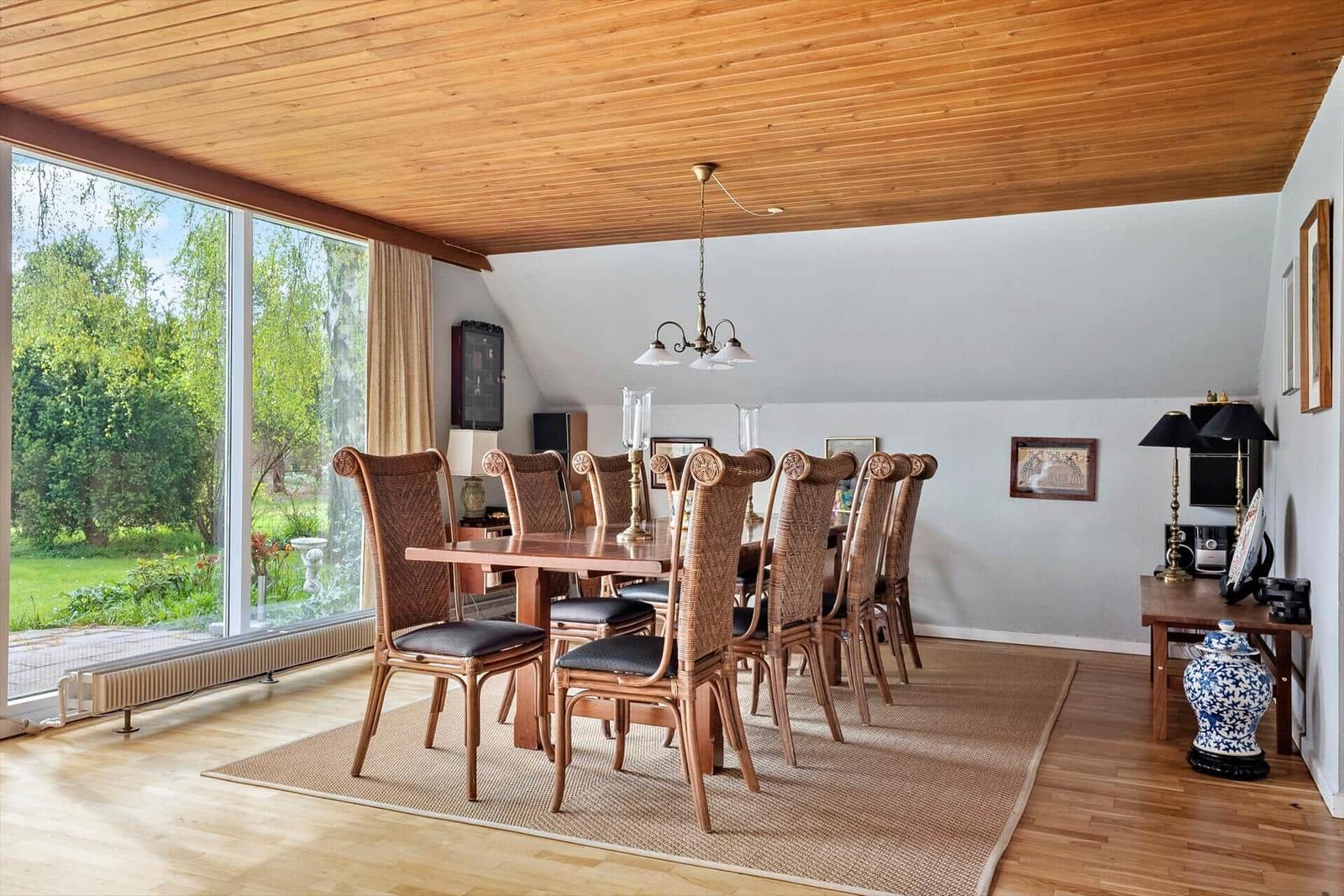 Esszimmer mit Holzdecke, großem Fenster und Esstisch mit acht Stühlen.