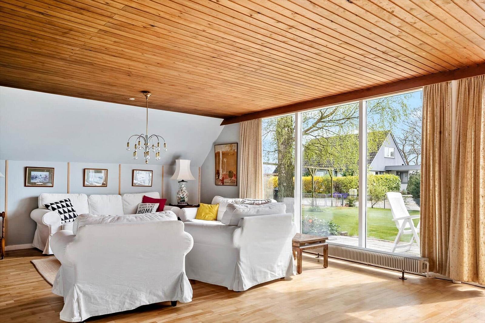 Wohnzimmer mit Holzdecke, weißen Sofas und großem Fensterblick auf Garten