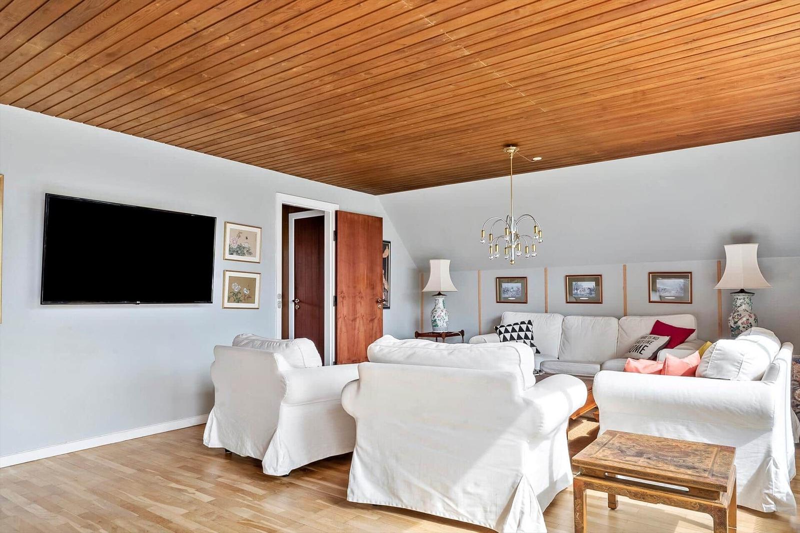 Wohnzimmer mit weißen Sesseln, Fernseher und Holzdecke.