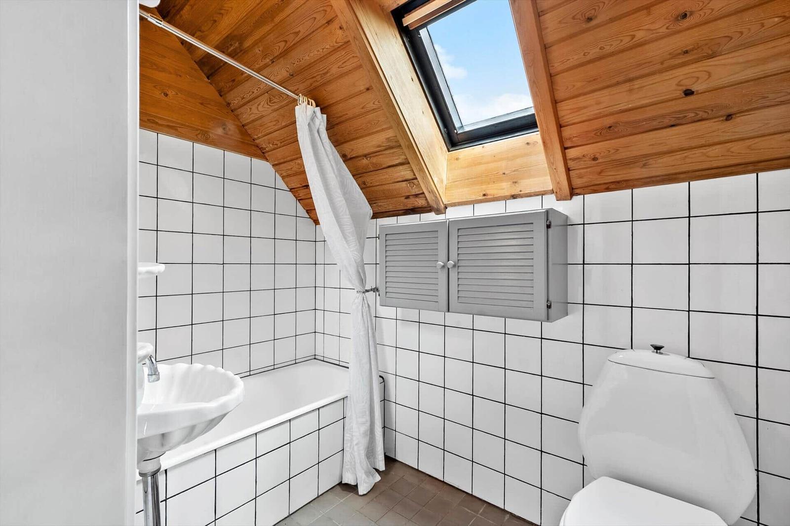 Badezimmer mit Dusche, Toilette und Waschbecken unter Holzdecke mit Dachfenster.