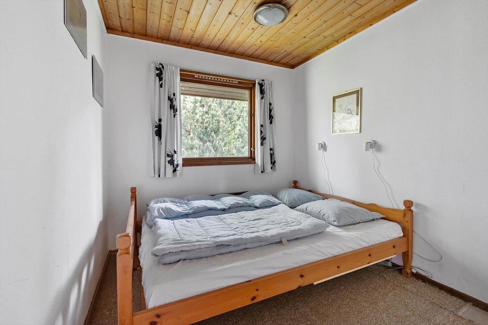 Schlafzimmer mit Holzbett, Fenster und Holzdecke.