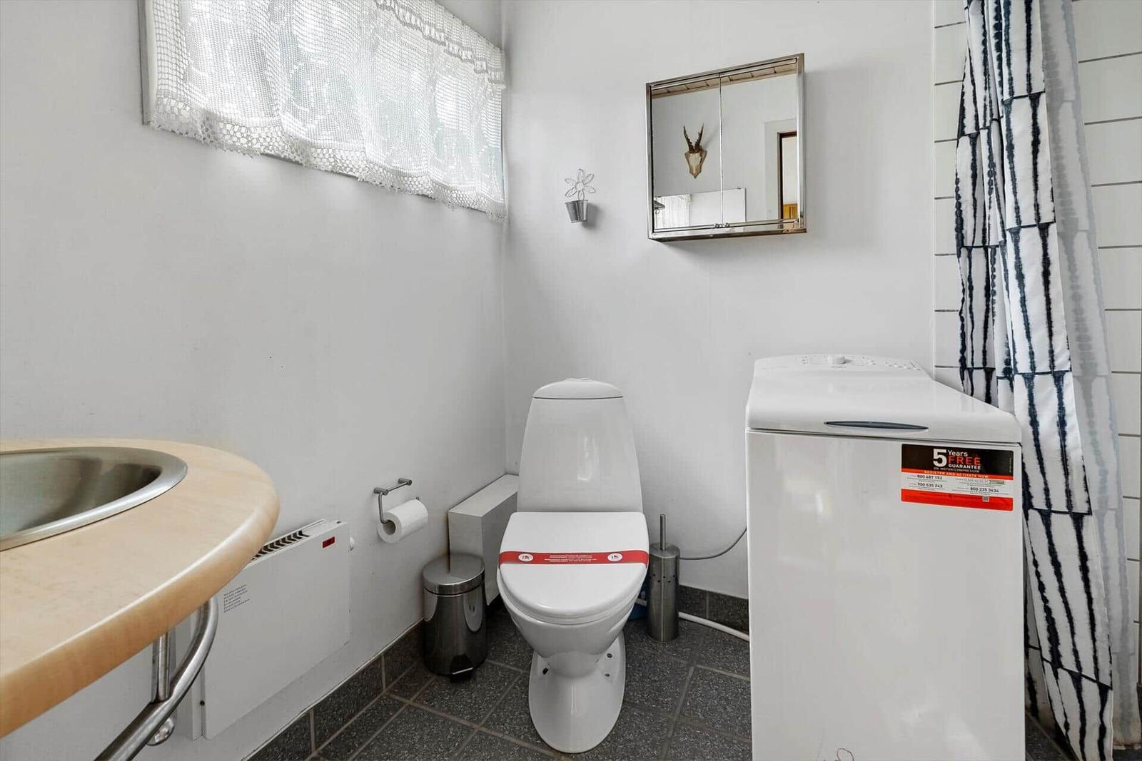 Badezimmer mit Toilette, Waschmaschine und Spiegel an der Wand.