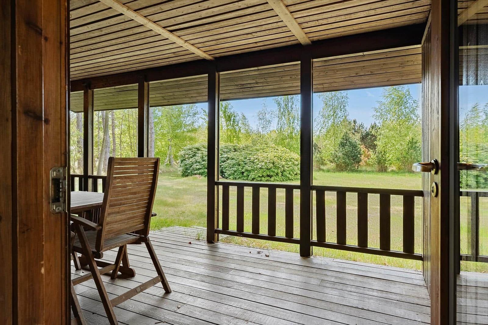 Terrasse mit Holztisch und Stuhl, Blick auf Grünfläche und Bäume.