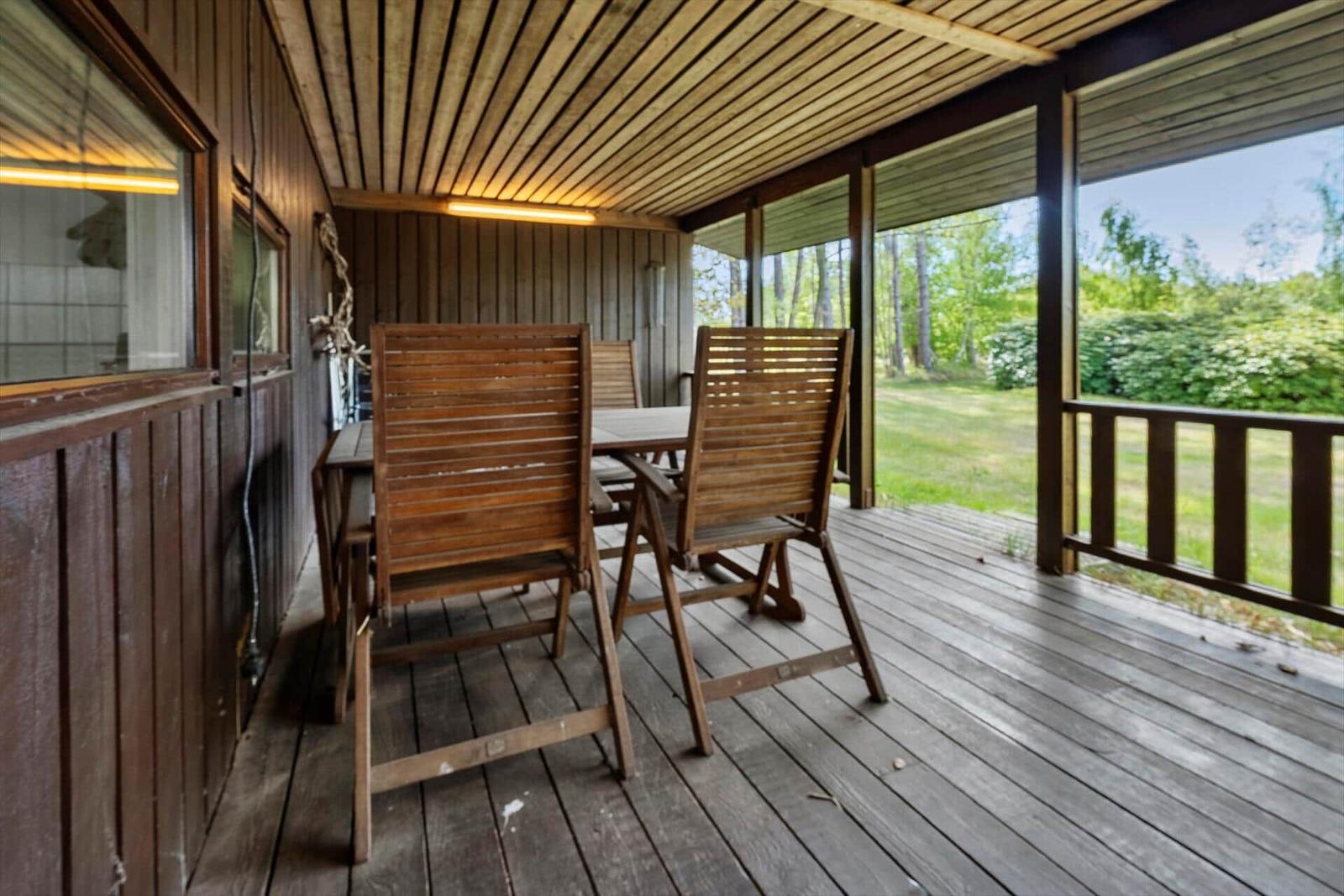 Holzterrasse mit Tisch und Stühlen, Blick auf grüne Wiese und Bäume.