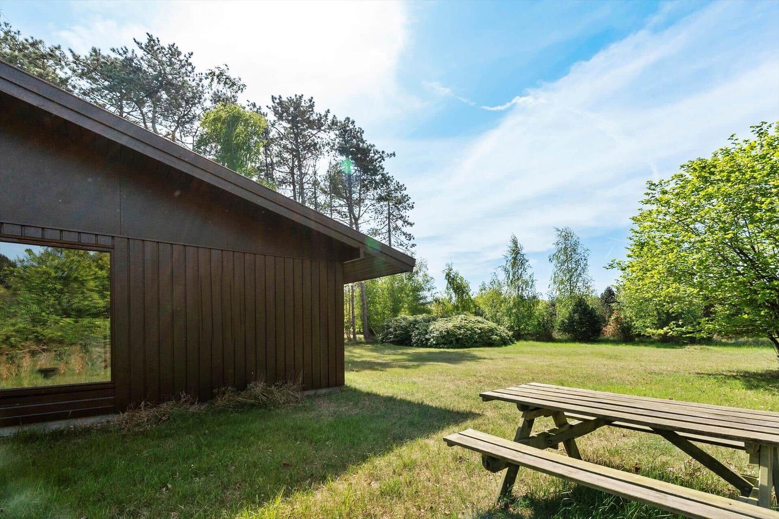 Holzhaus mit Picknicktisch im Garten unter Bäumen.