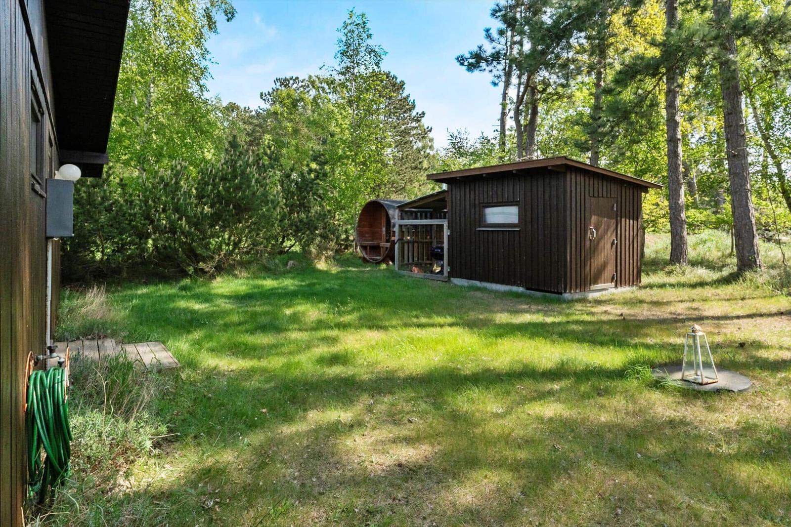 Hinterhof mit Holzhaus, Grillplatz und grünem Rasen im Wald.